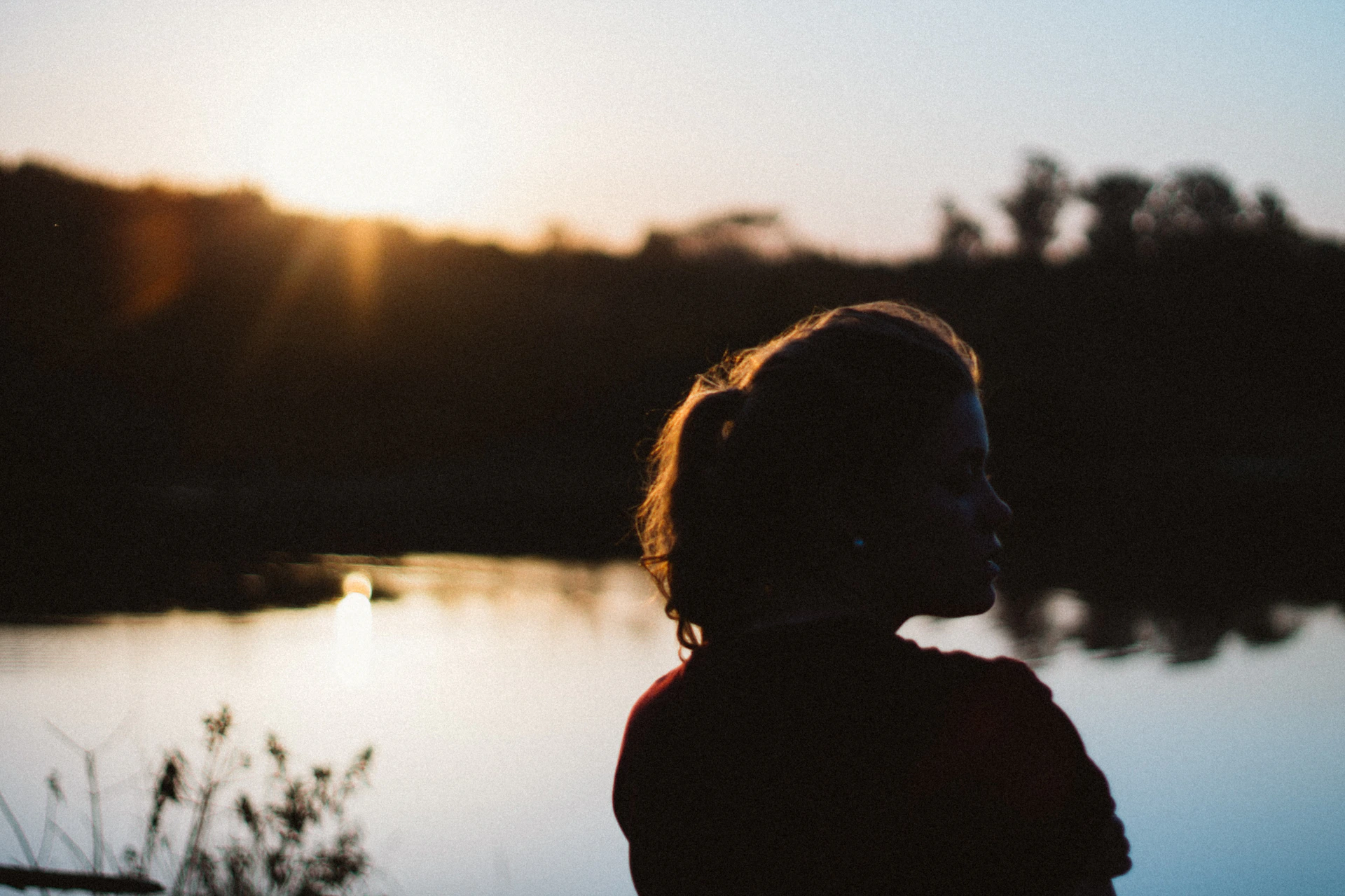 Silhouette of a woman against a sunset over water.