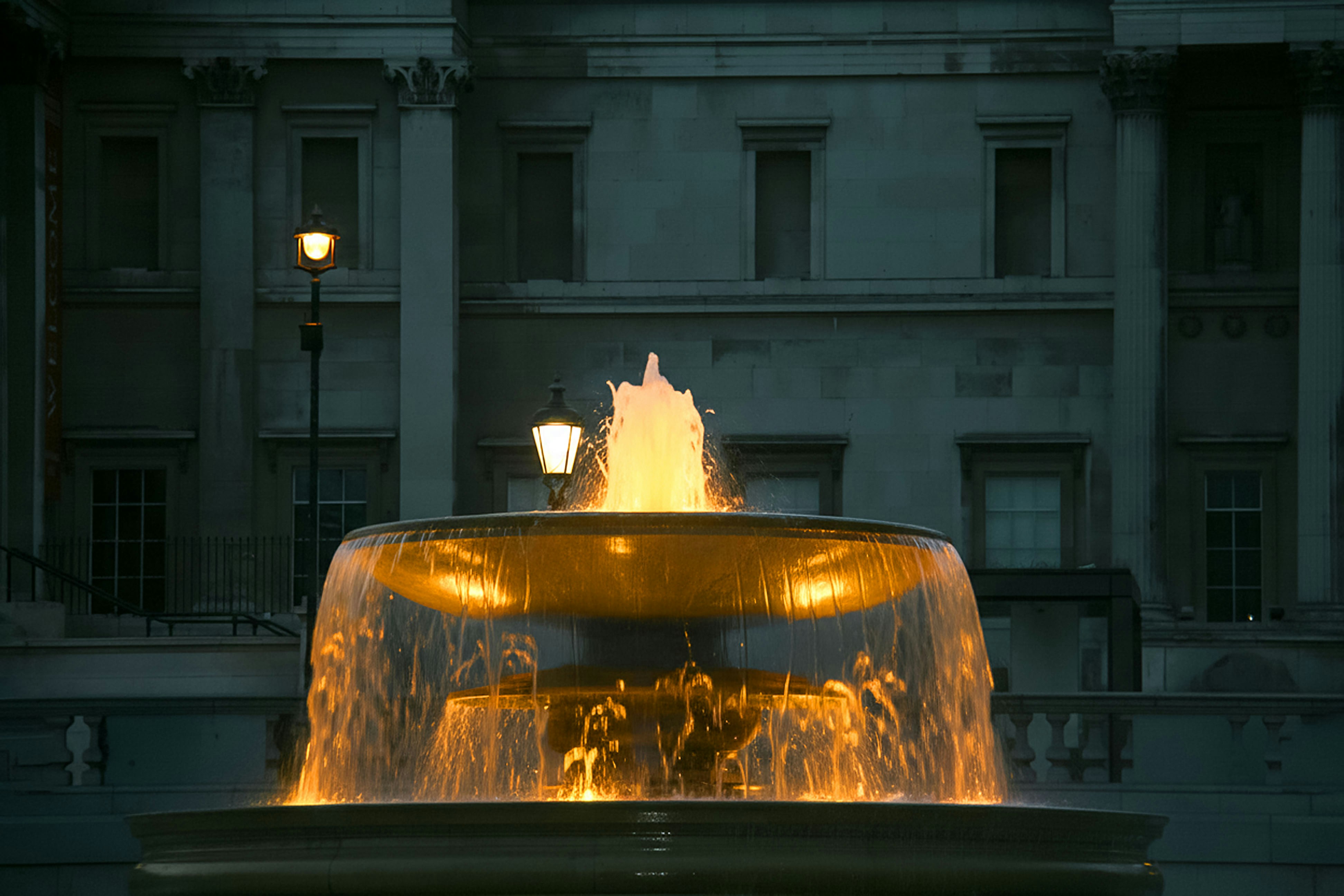 Lit fountain with water cascading down tiers at dusk.