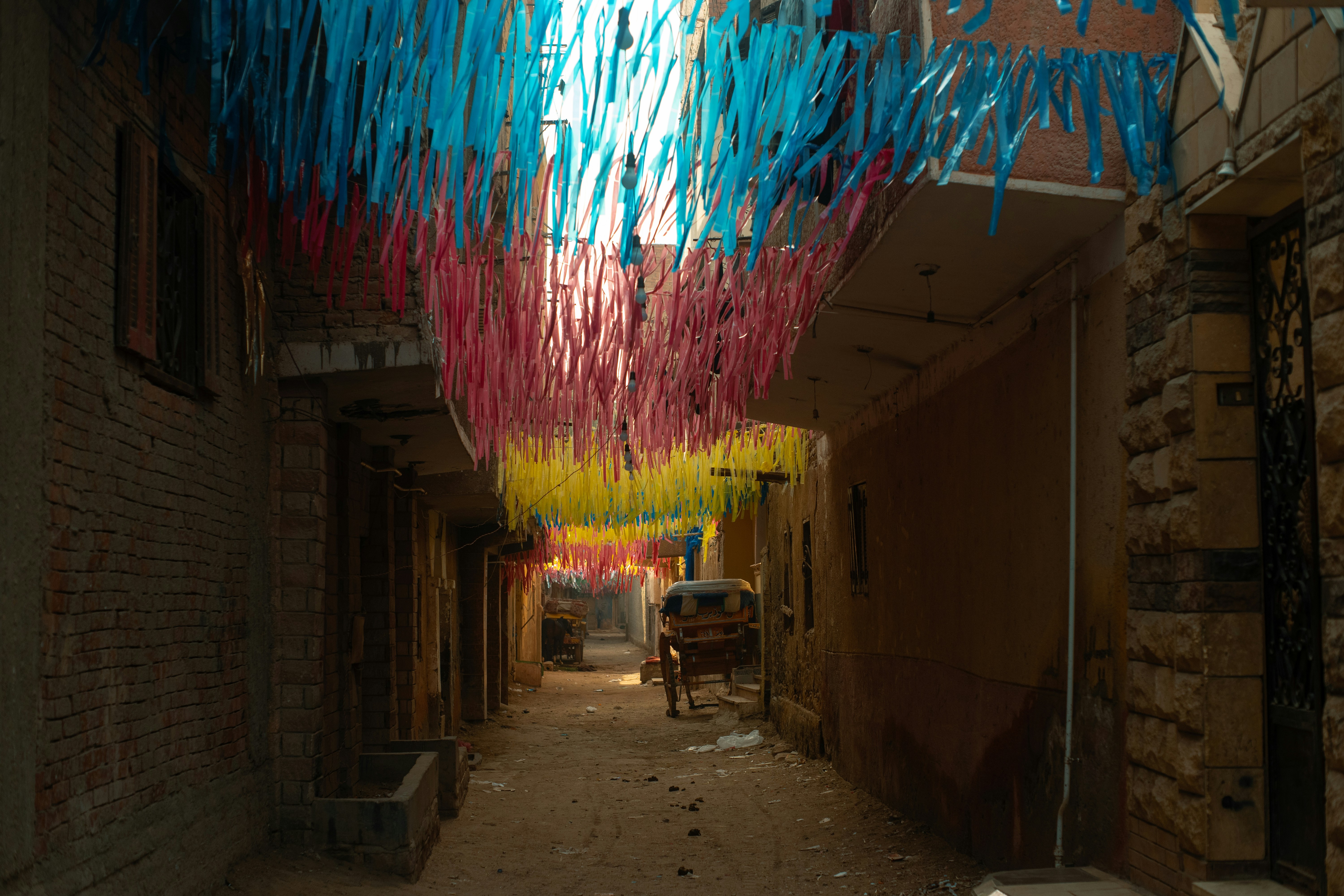 Colorful streamers hang over a narrow street with a vehicle.