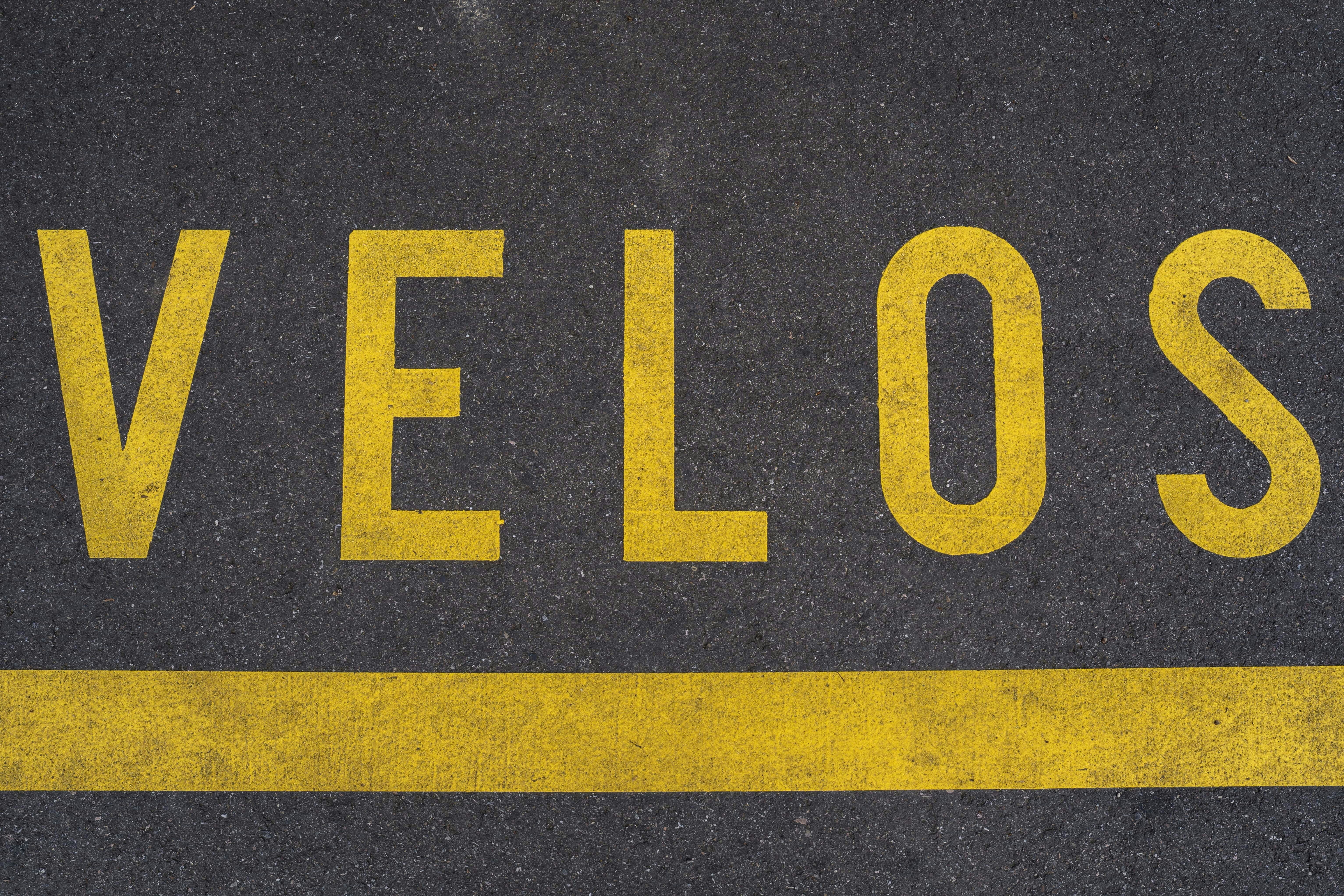 Yellow letters spelling velos on asphalt