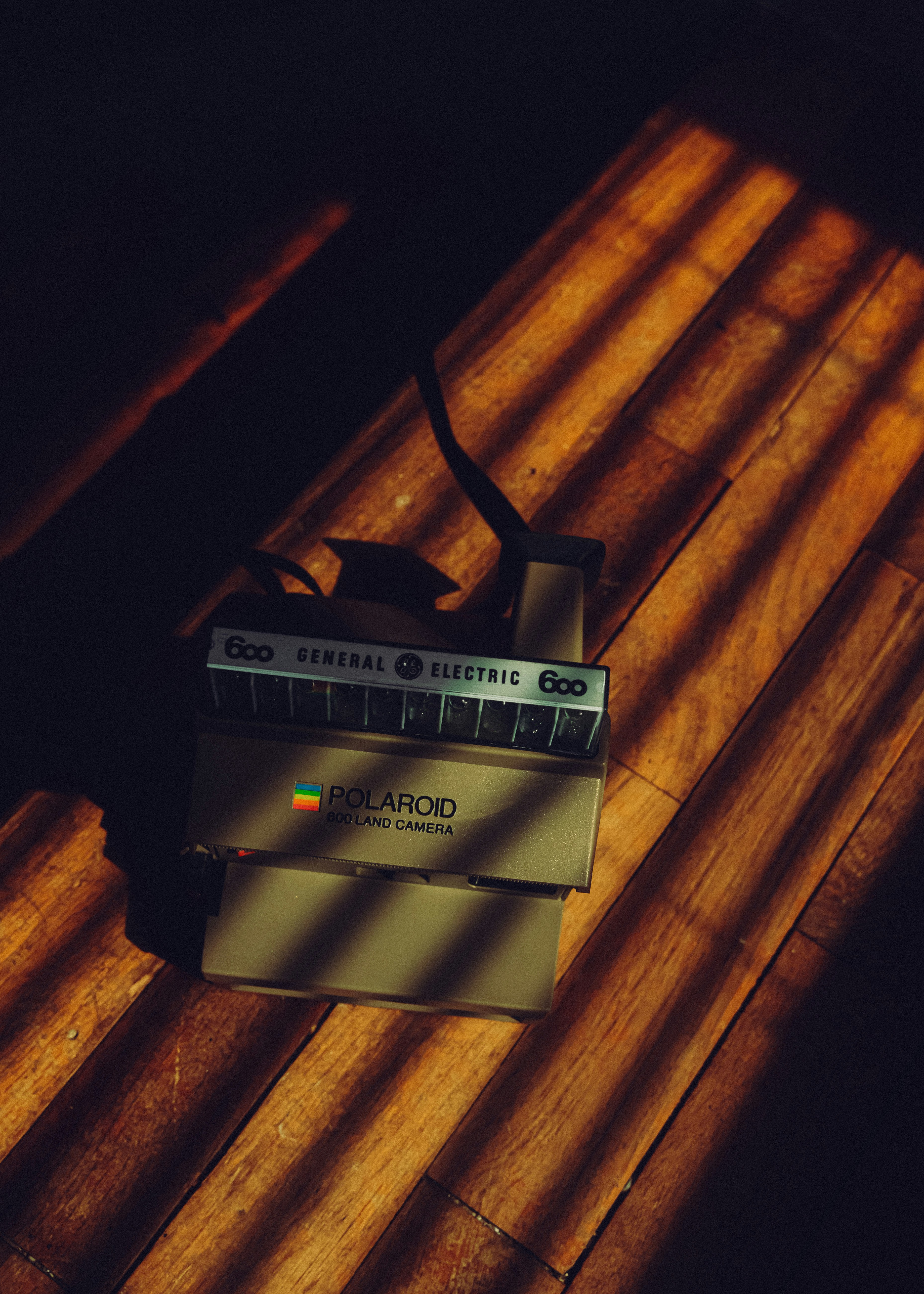 Vintage polaroid camera on wooden floor with shadows.