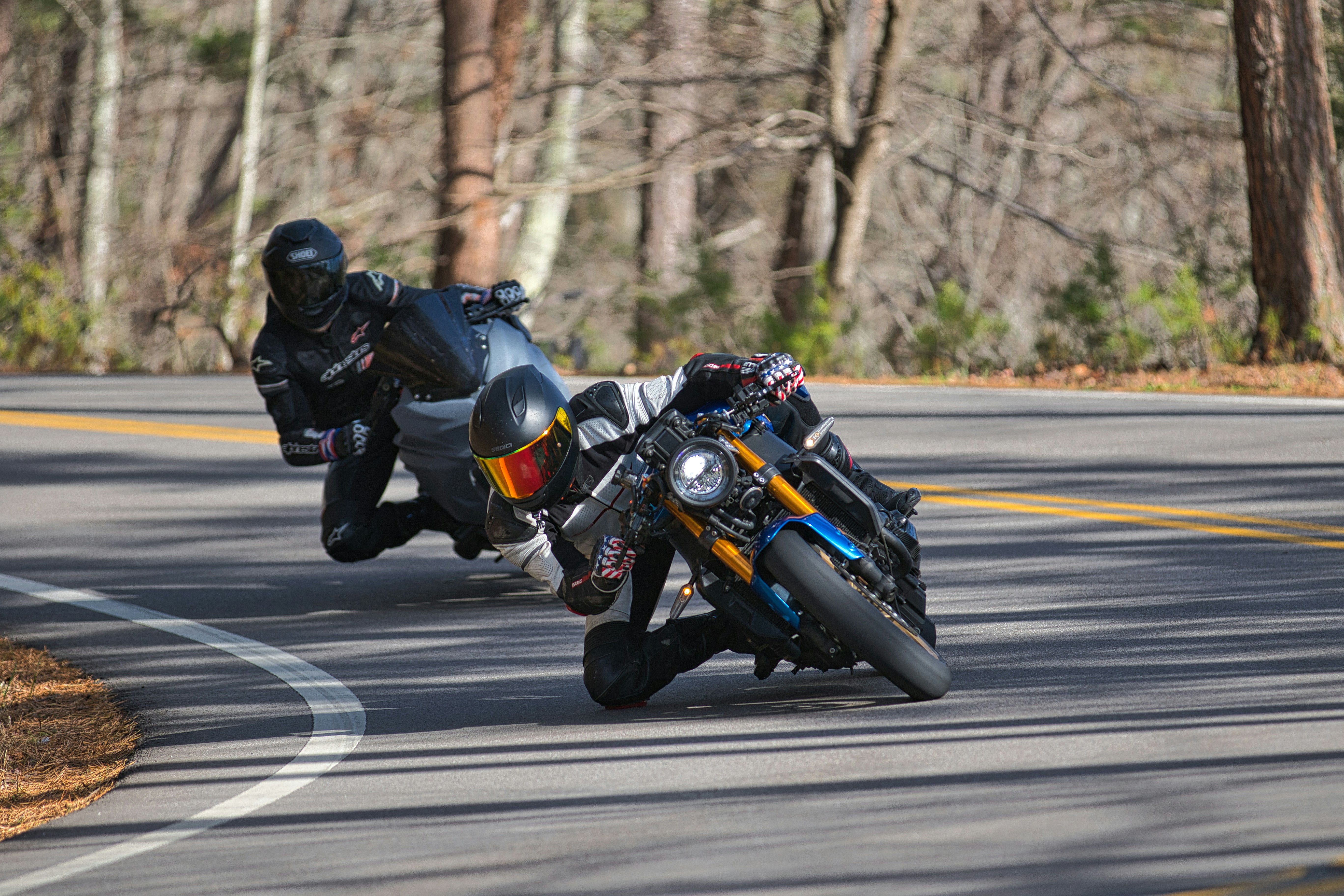 Two motorcyclists leaning into a sharp turn on a road.