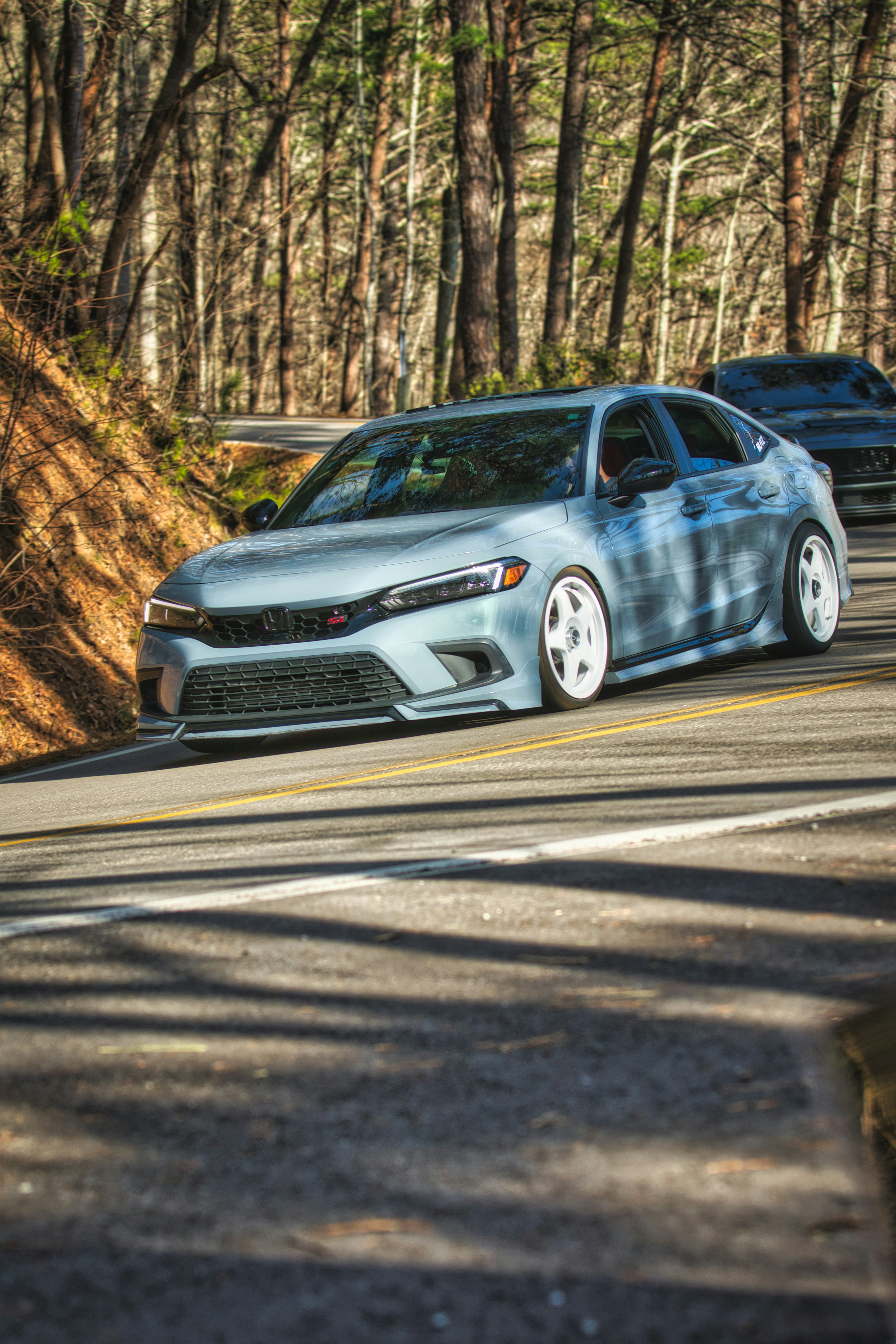 Ein hellblaues Auto fährt eine kurvenreiche Waldstraße entlang.