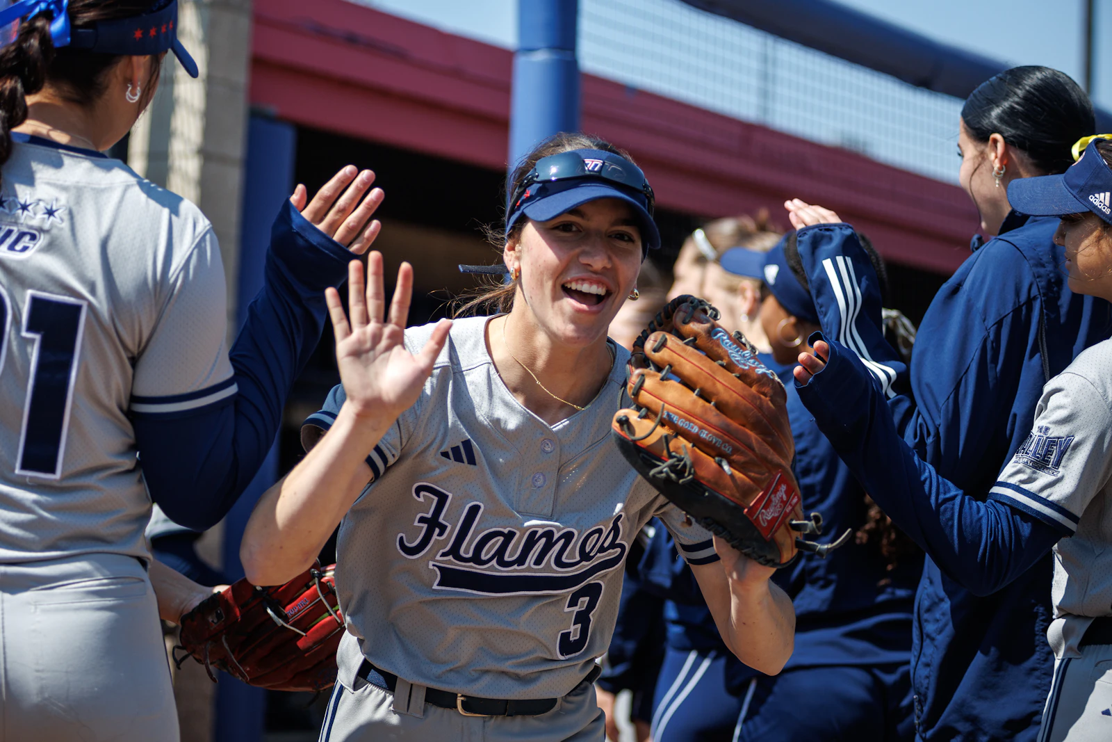 A women's sports team in matching uniforms high-fiving and celebrating together in a dugout