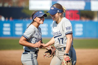 Two smiling women in softball uniforms on field