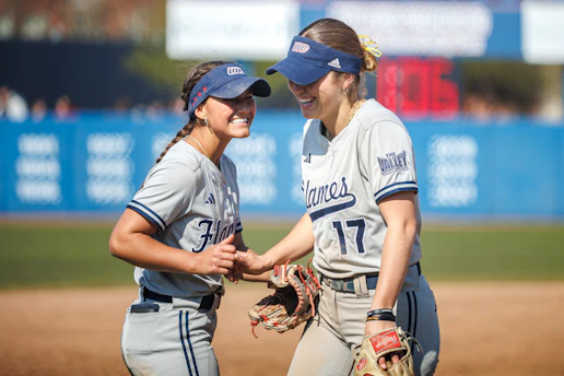 Two smiling women in softball uniforms on field
