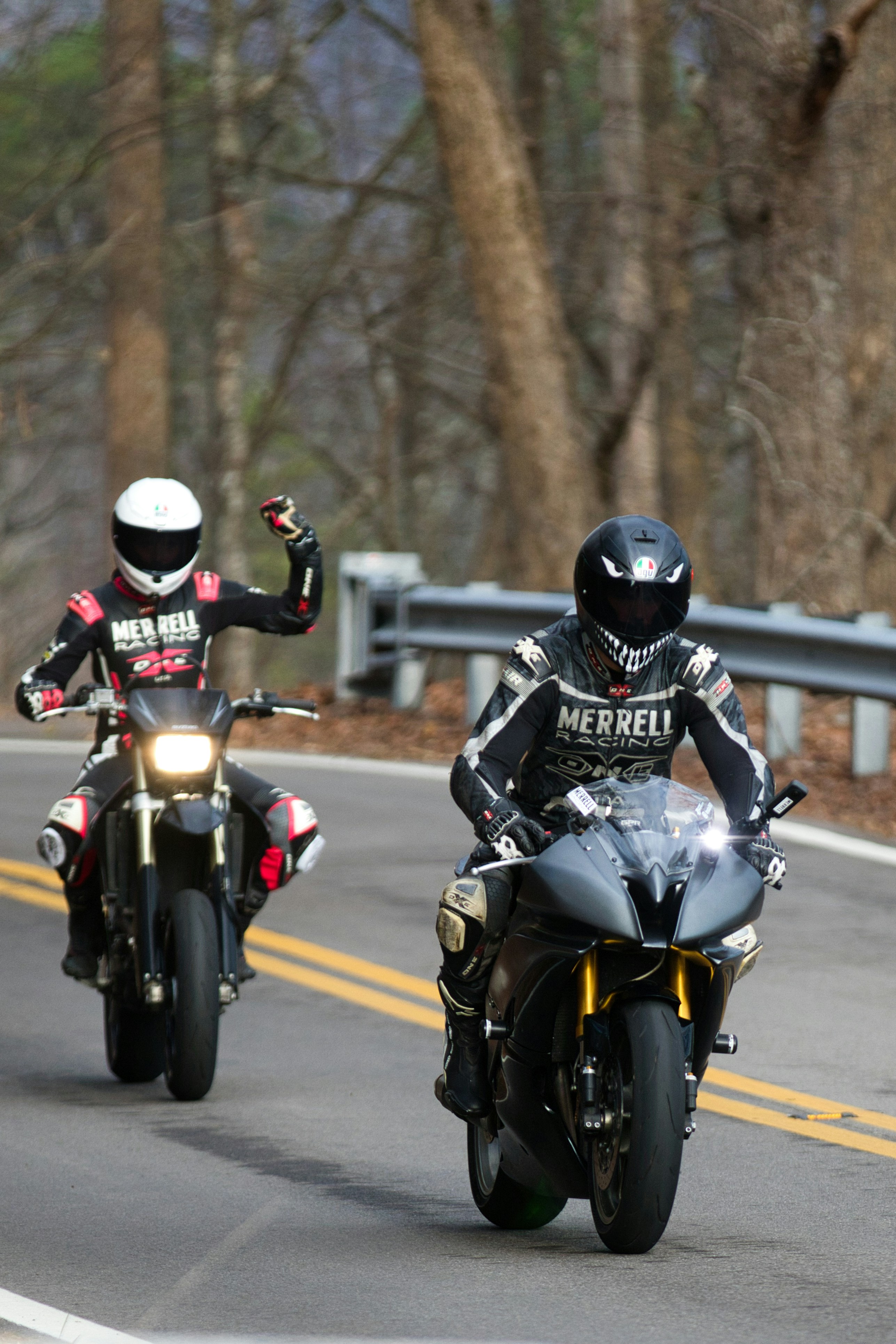 Two motorcycle riders wearing helmets and full protective riding gear on a winding outdoor road