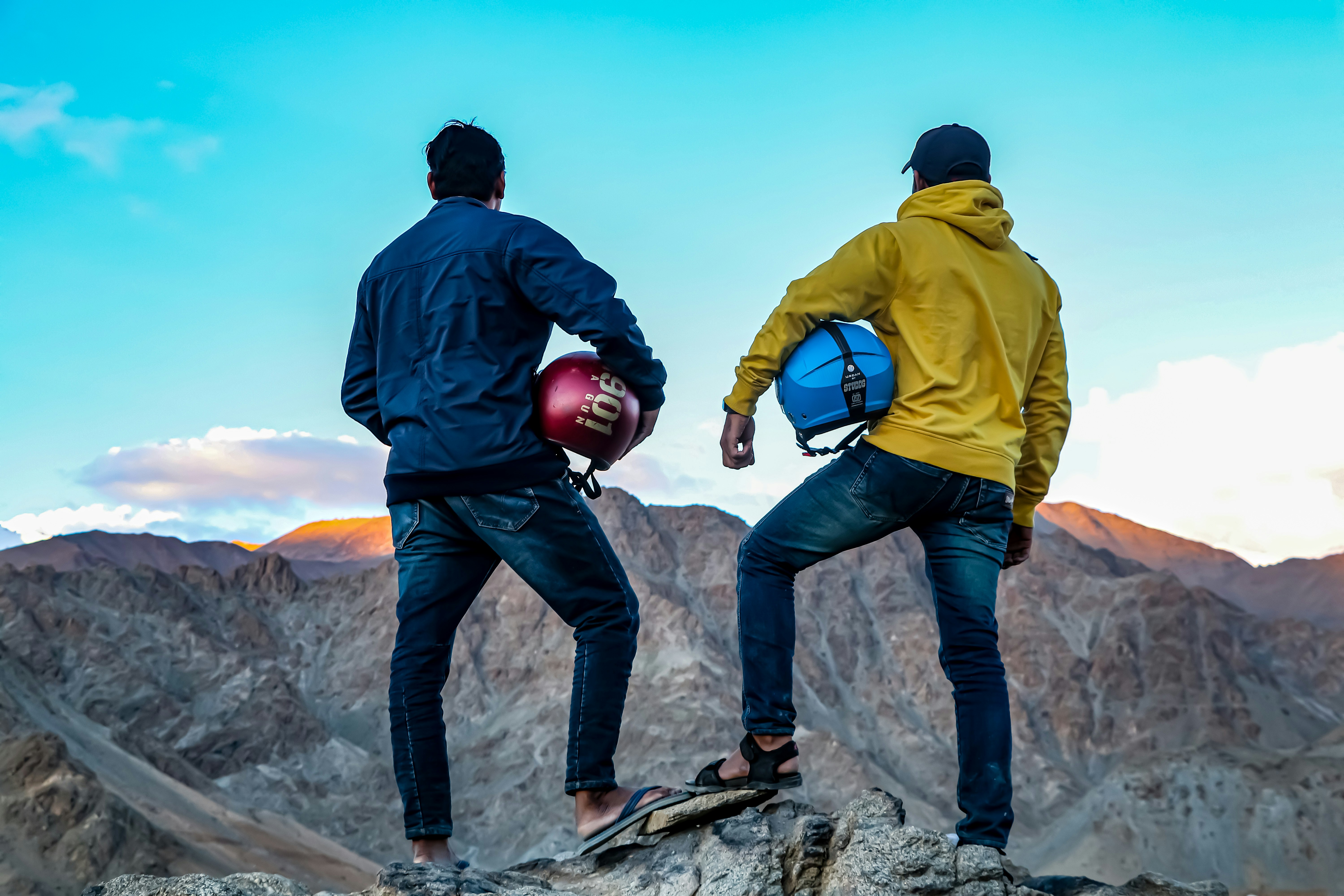 Two men holding helmets on a mountain peak.