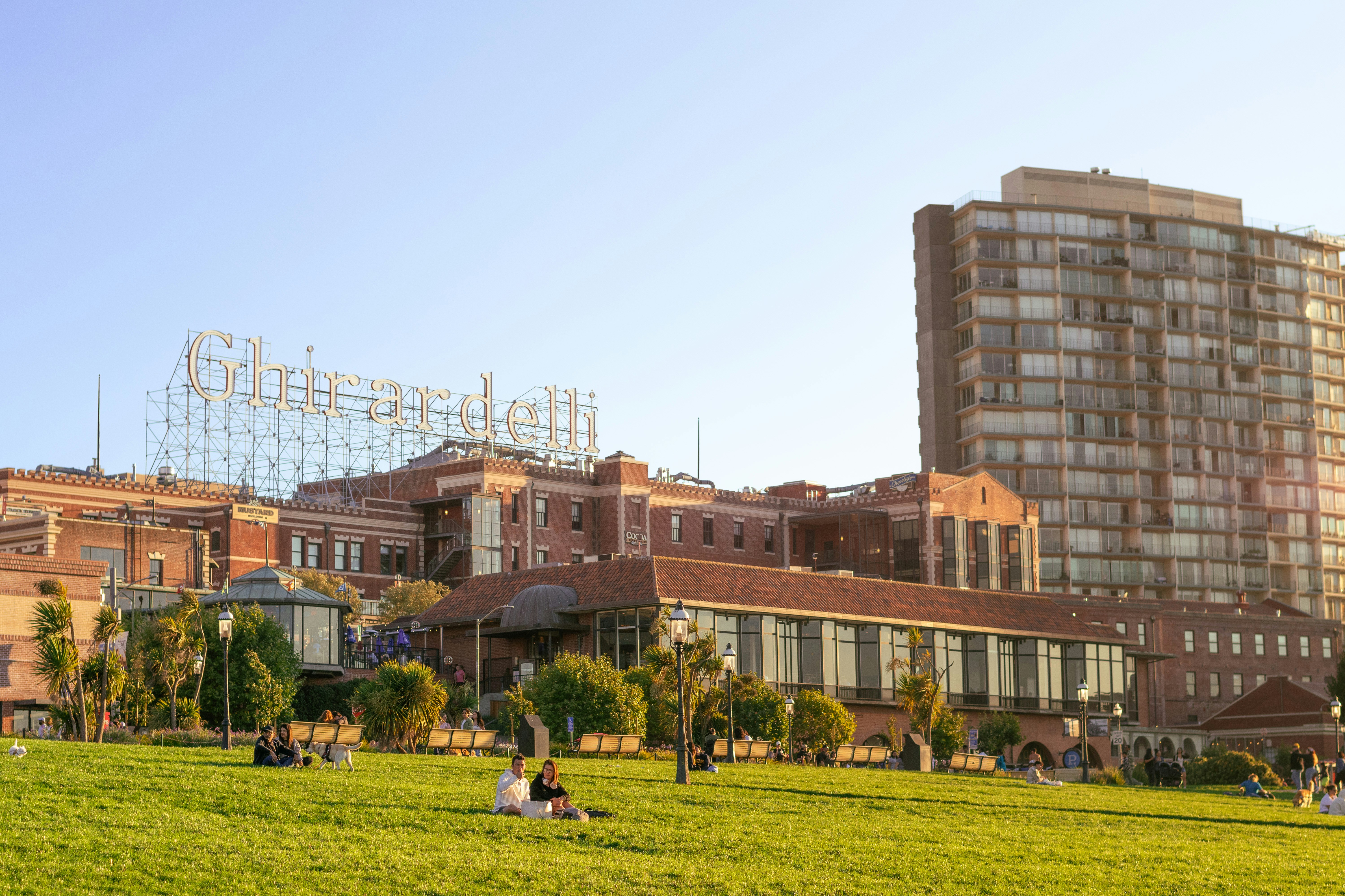 People relaxing on a grassy hill with city buildings behind.