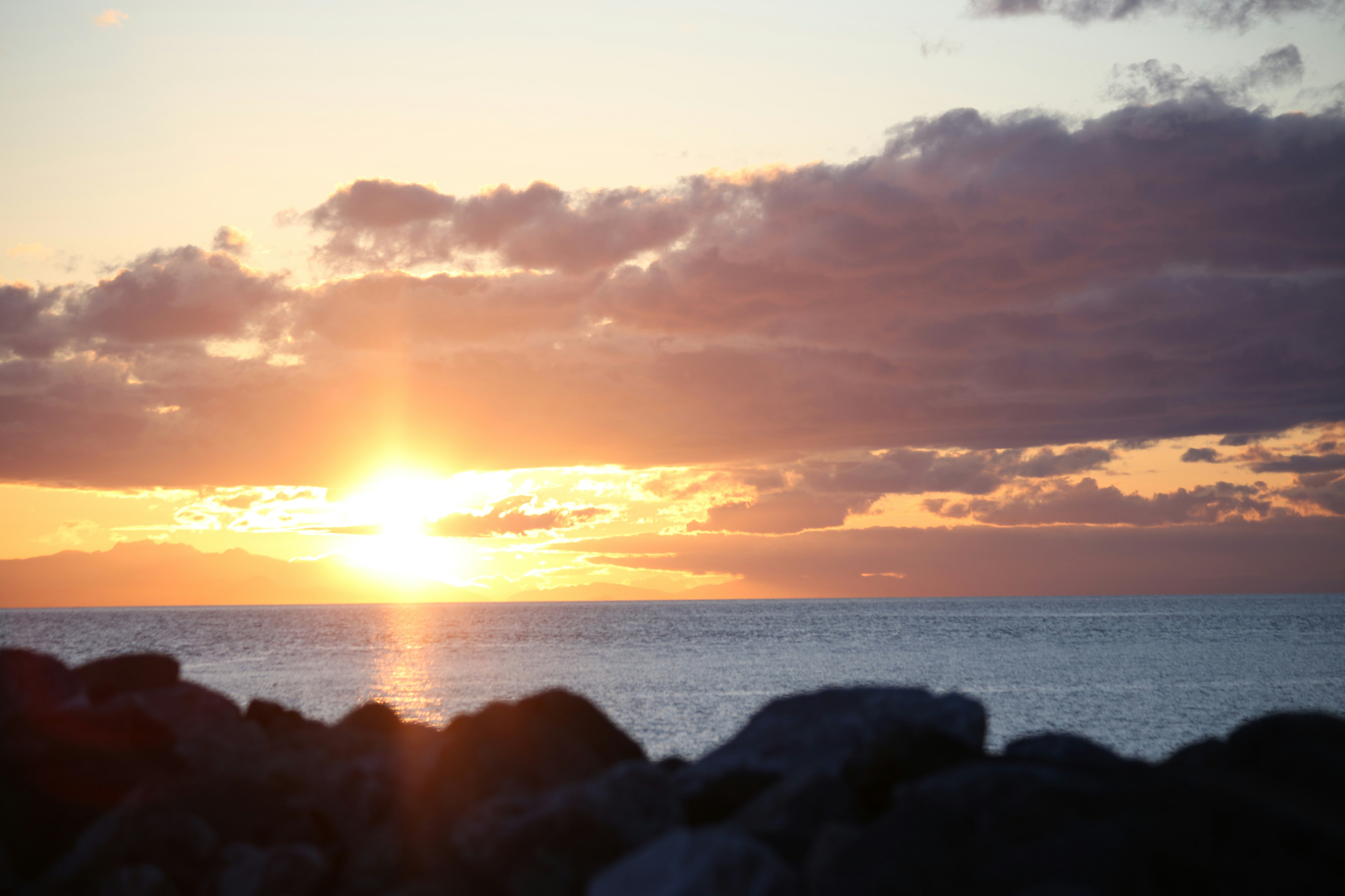 Sunset over the ocean with rocks in foreground
