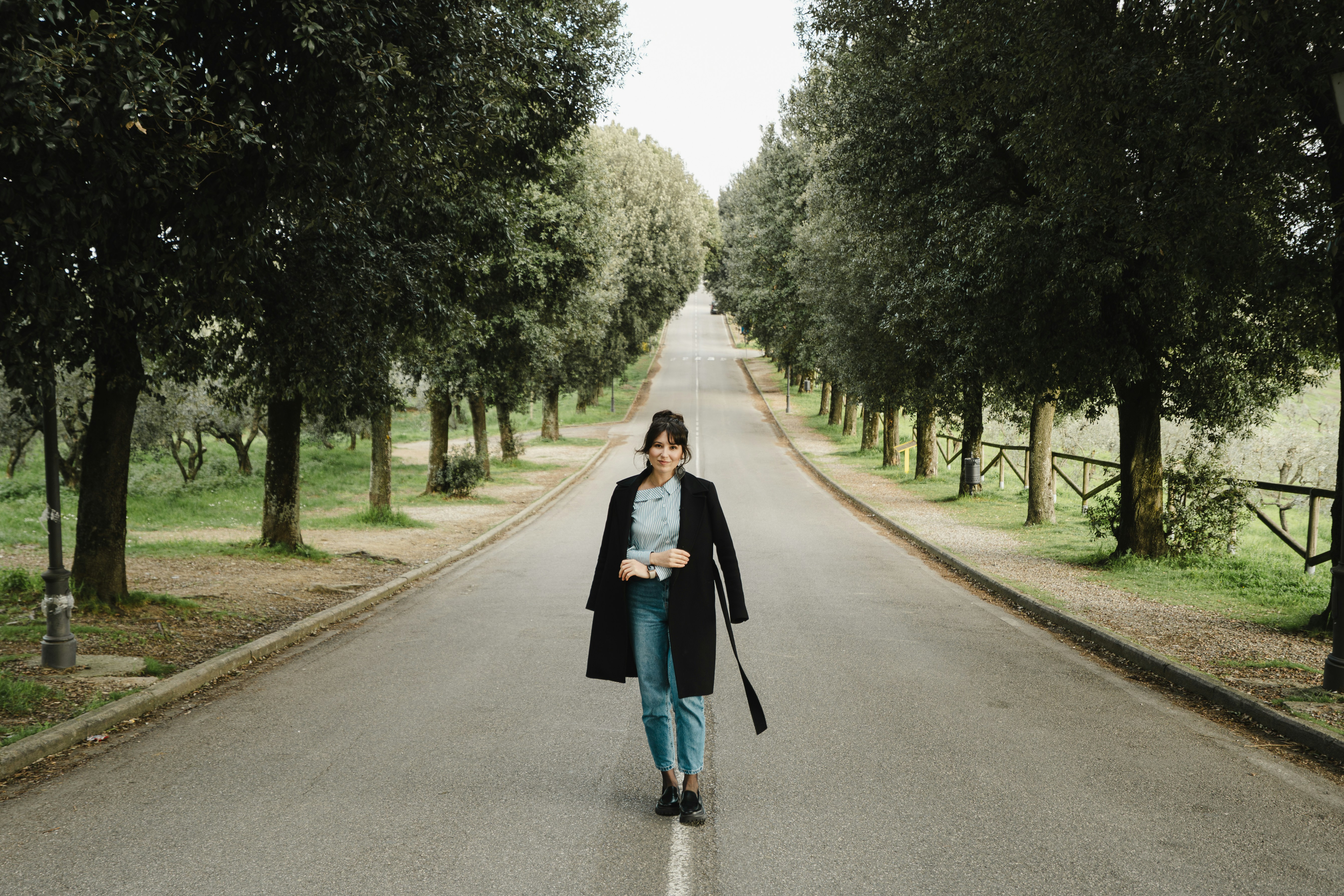 A woman walks down a tree-lined road