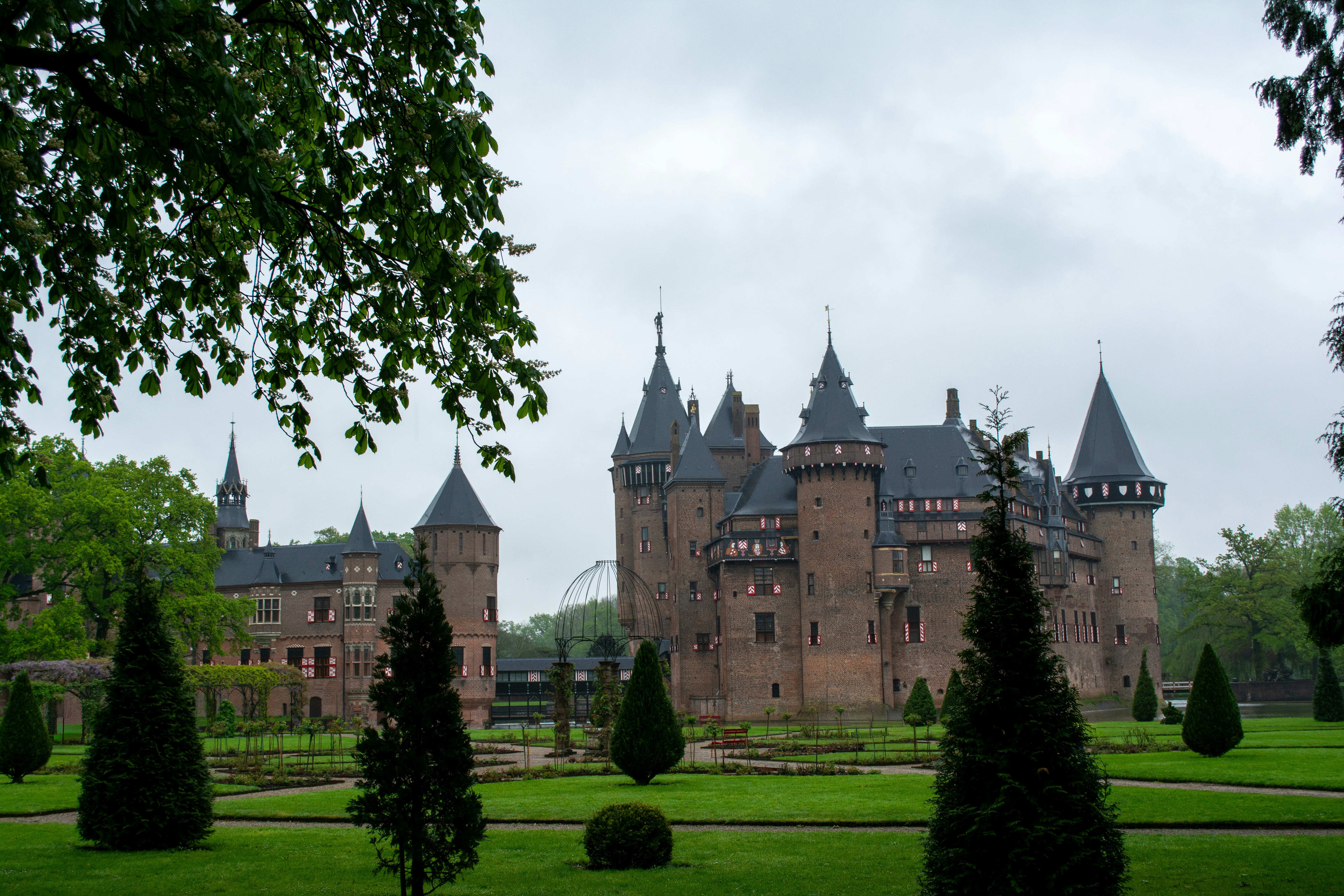 Un gran castillo de ladrillo con múltiples torres y jardines cuidados.