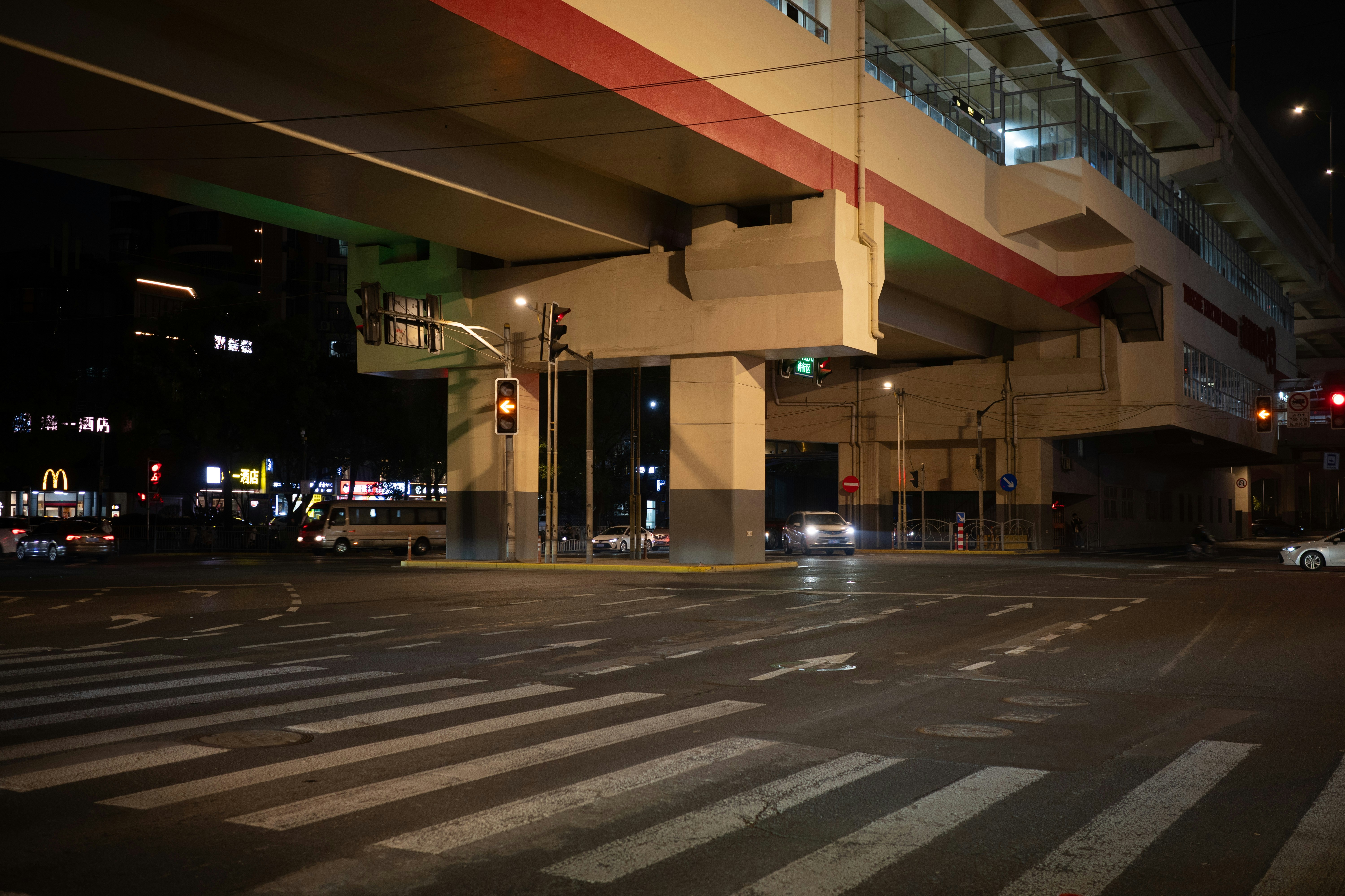 Cars drive under a highway overpass at night.