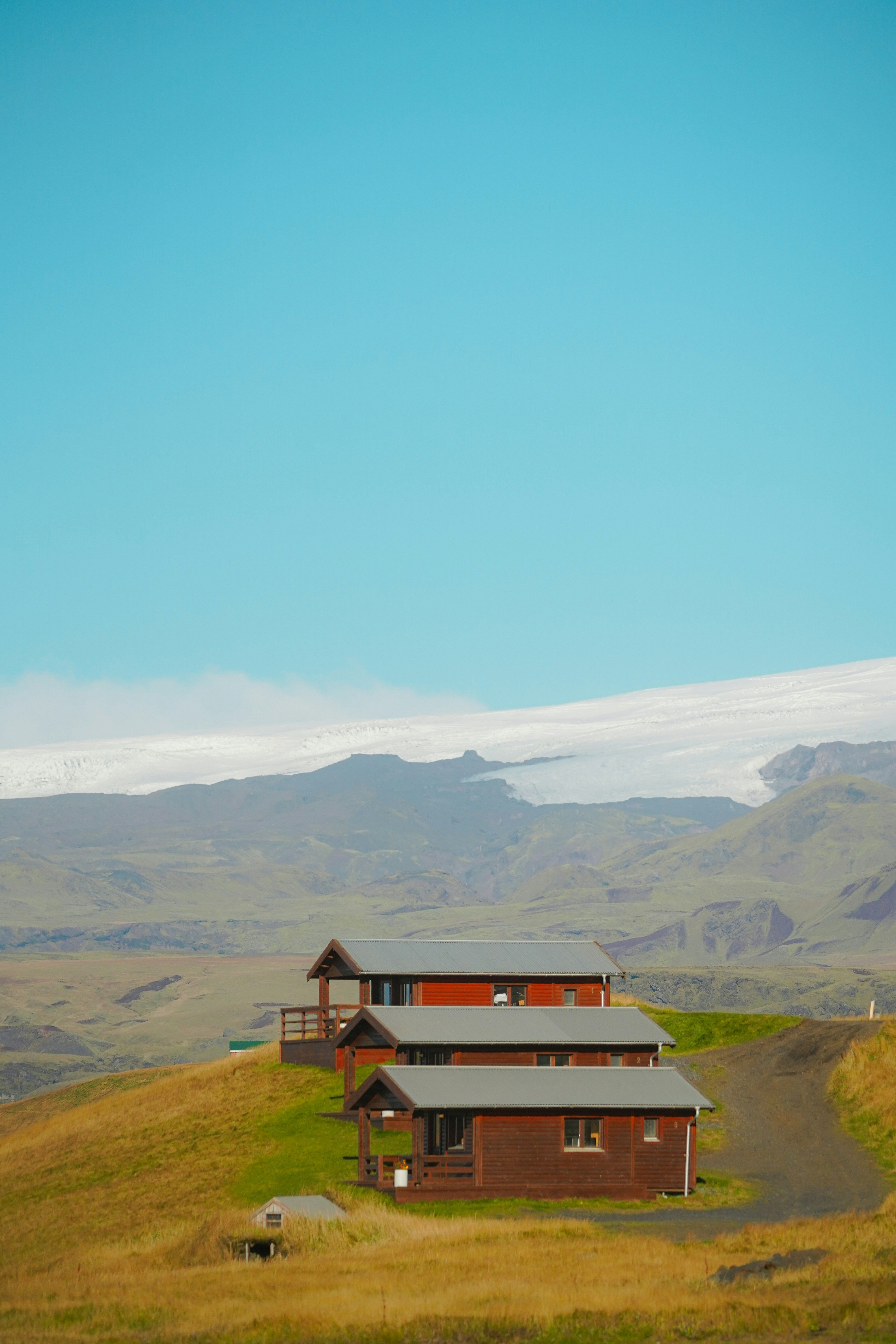Three cabins on a grassy hill with mountains behind