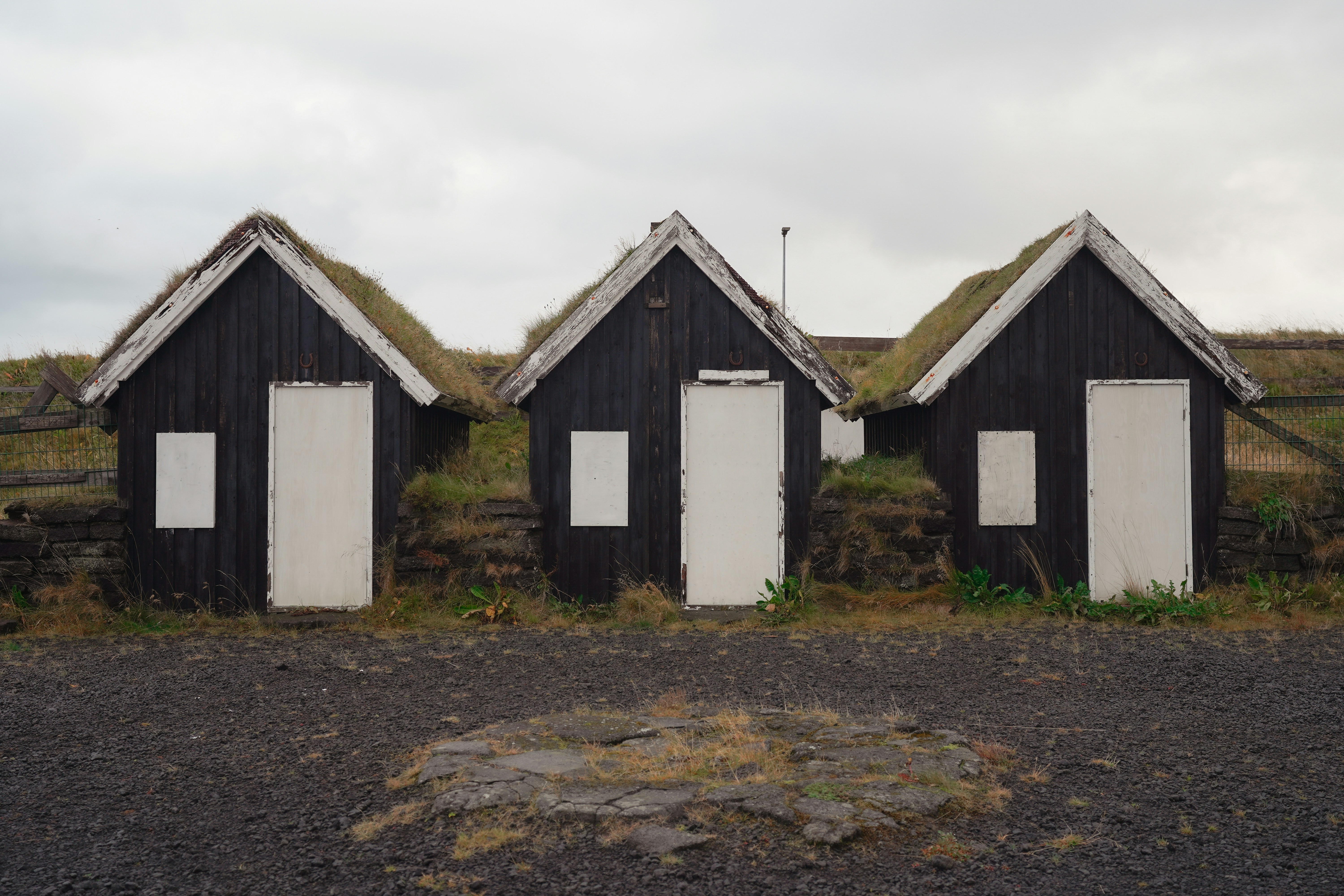 Three small black houses with grass roofs