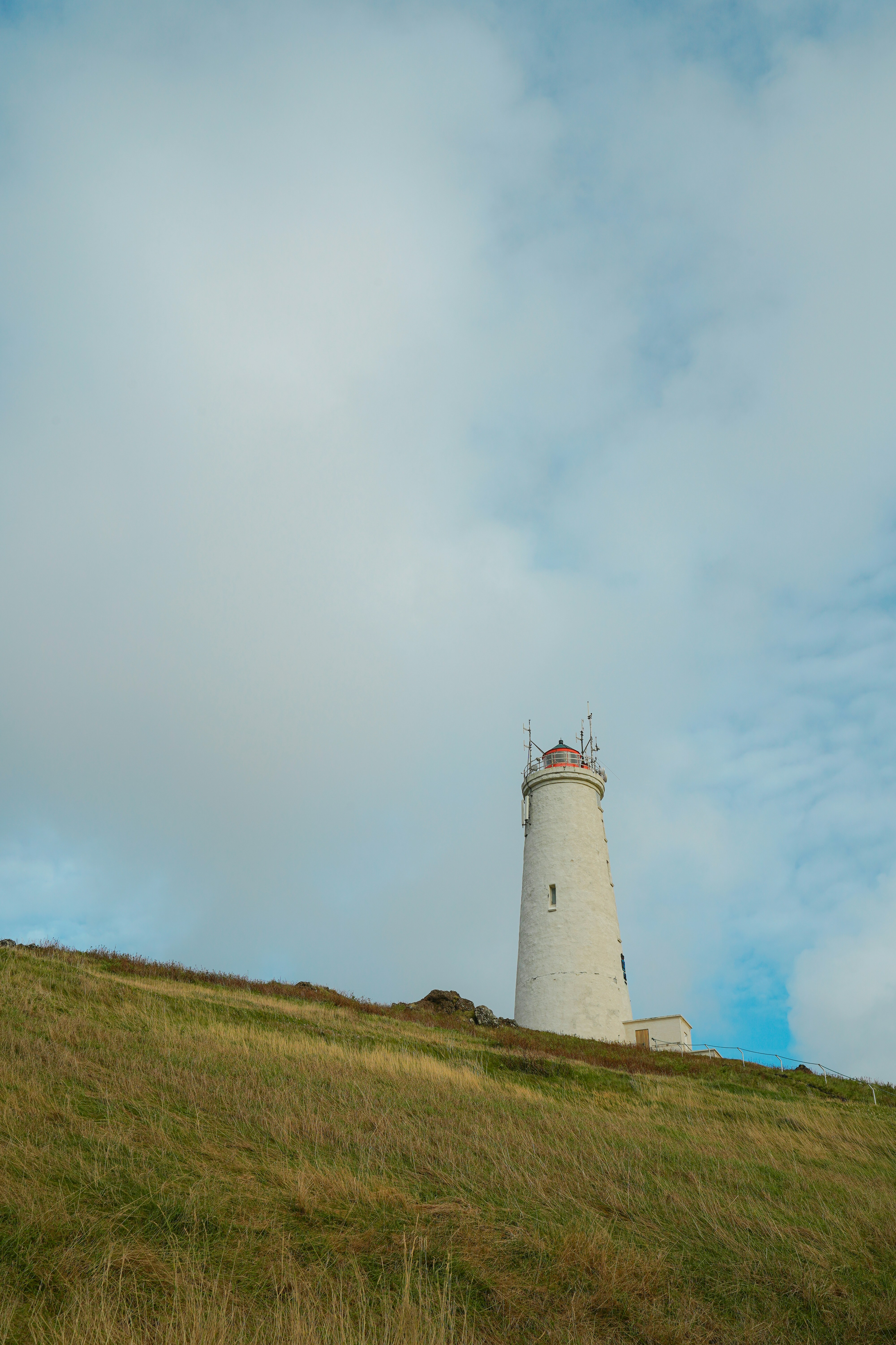White lighthouse on a grassy hill under cloudy sky