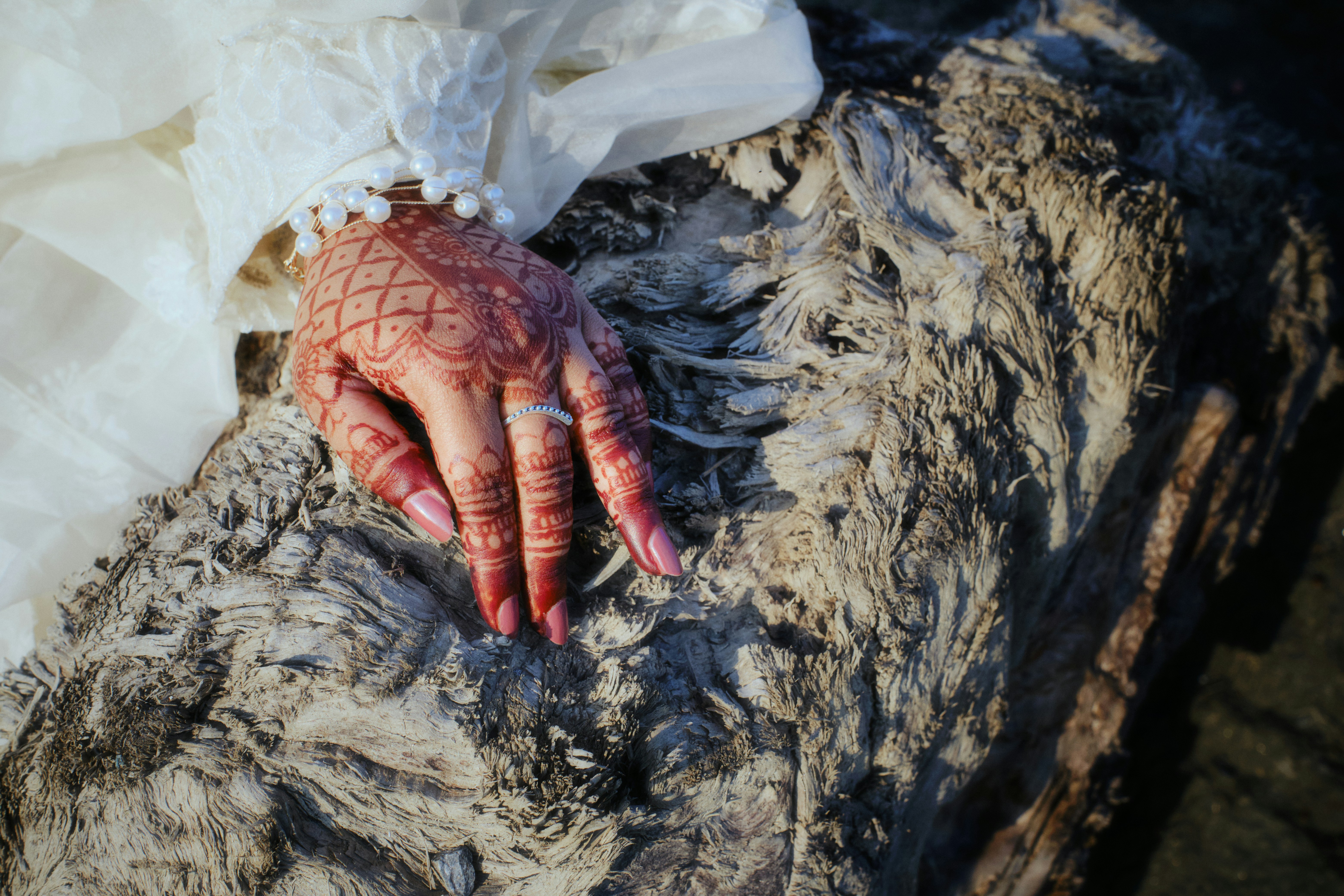 A hand with henna and rings rests on rough material.