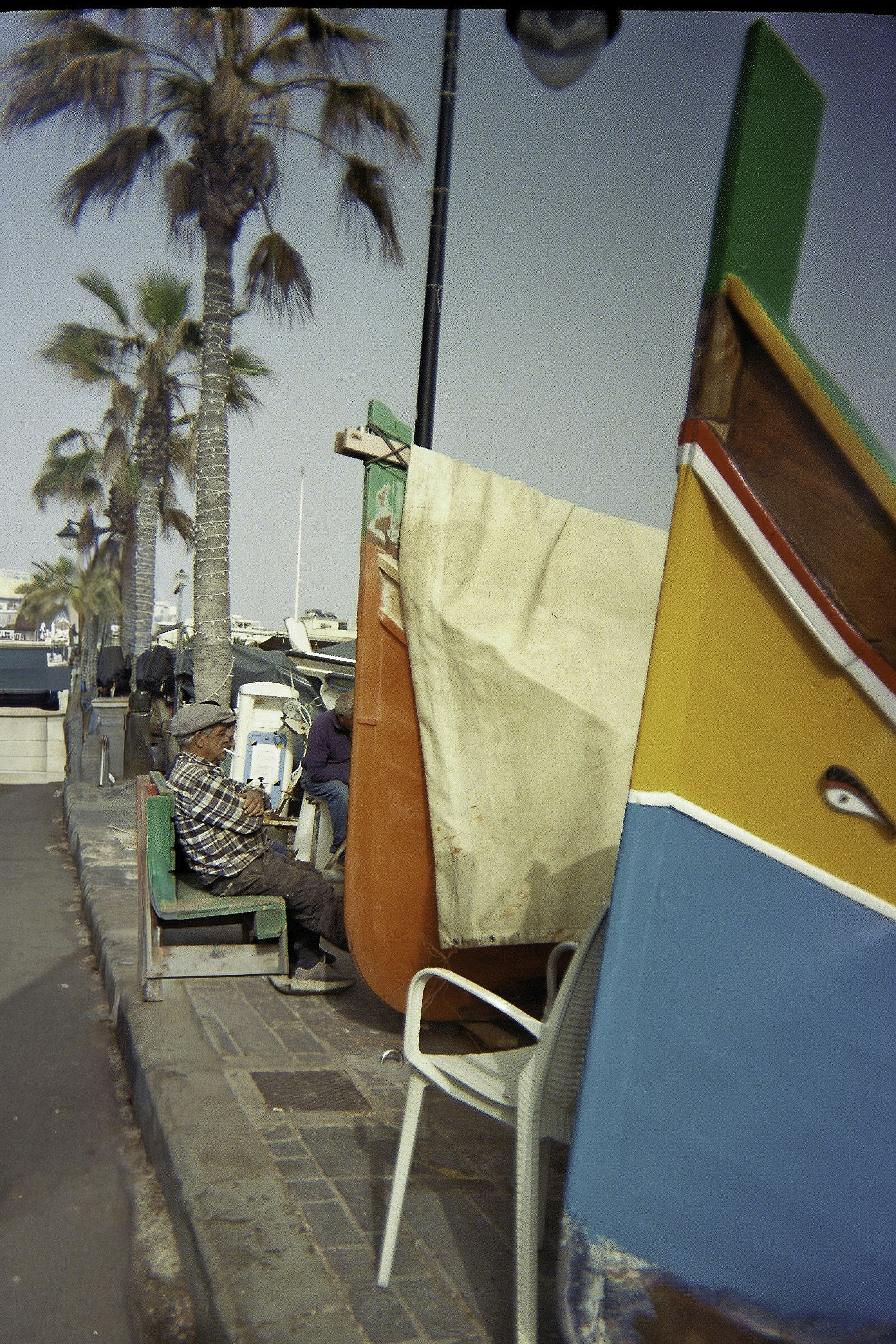 Man sleeping on bench beside colorful boats