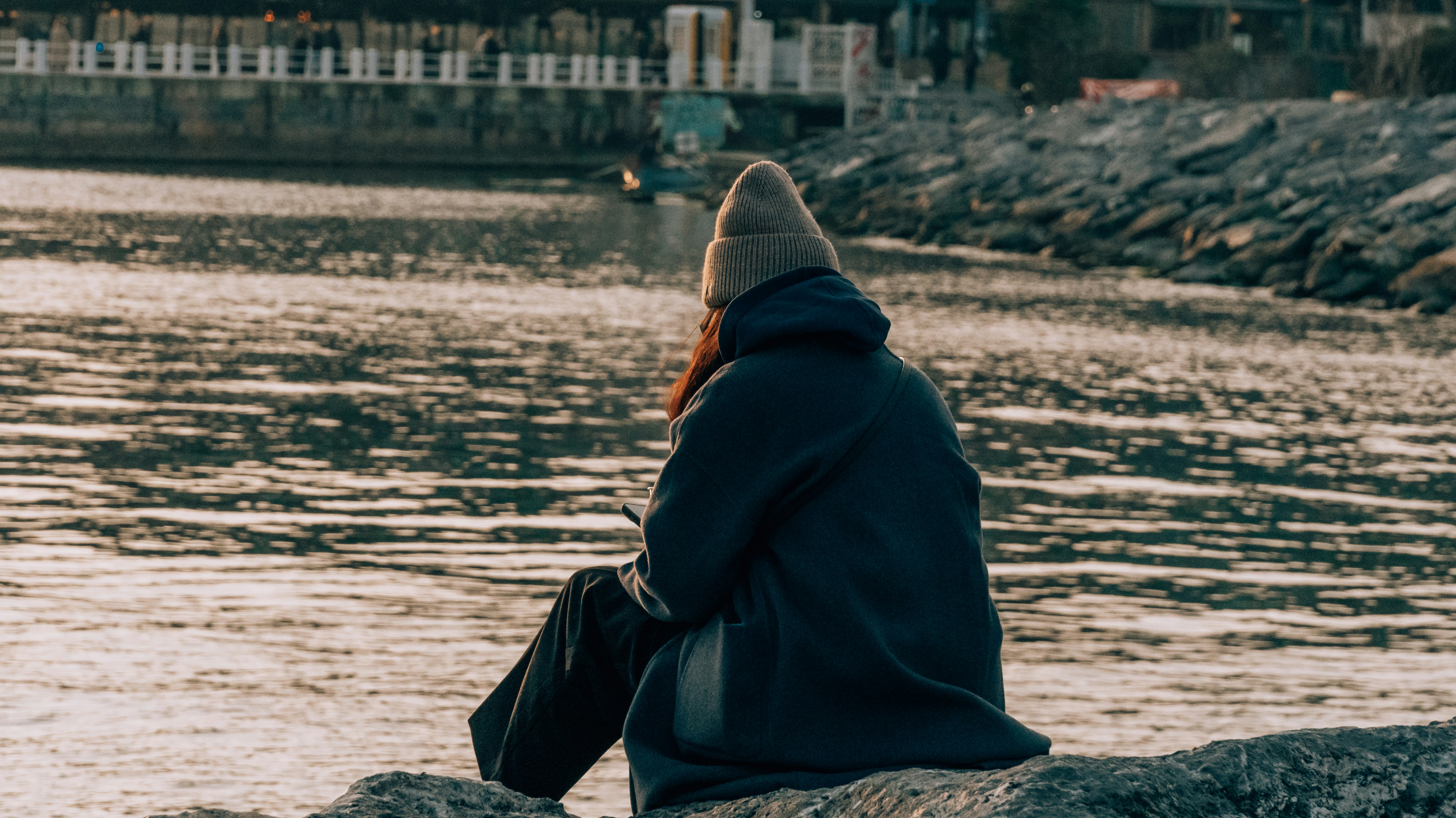 Person in beanie sits by the water