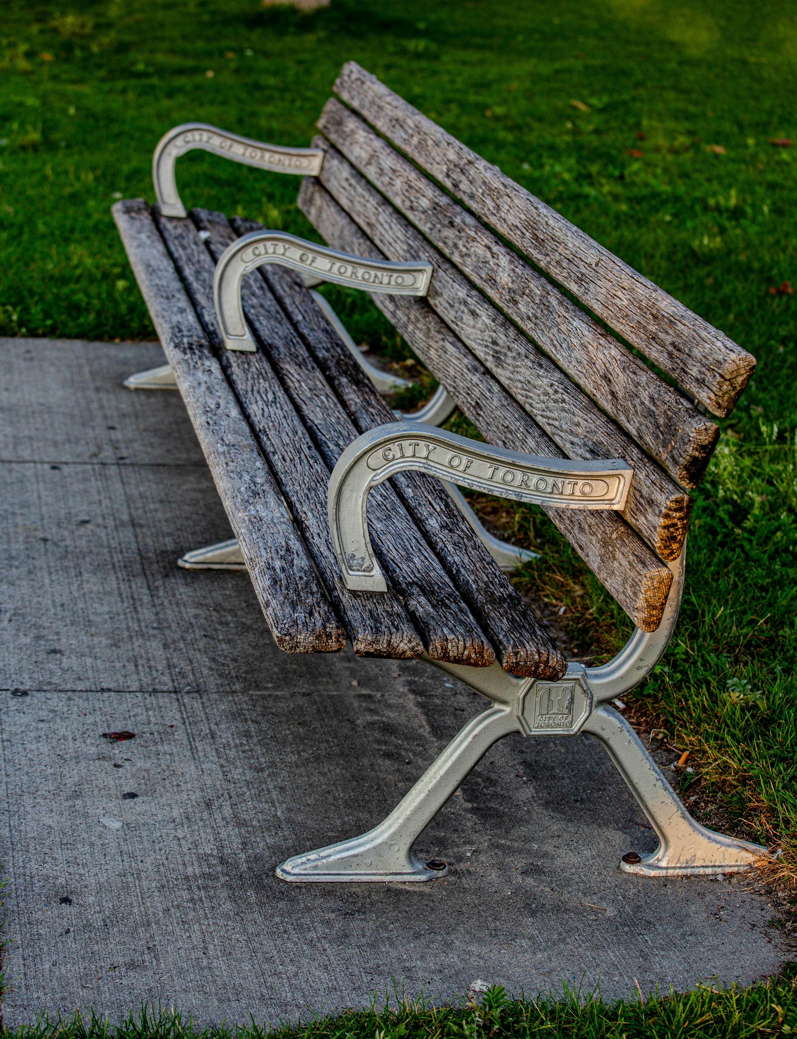 An old wooden park bench sits on a concrete path.