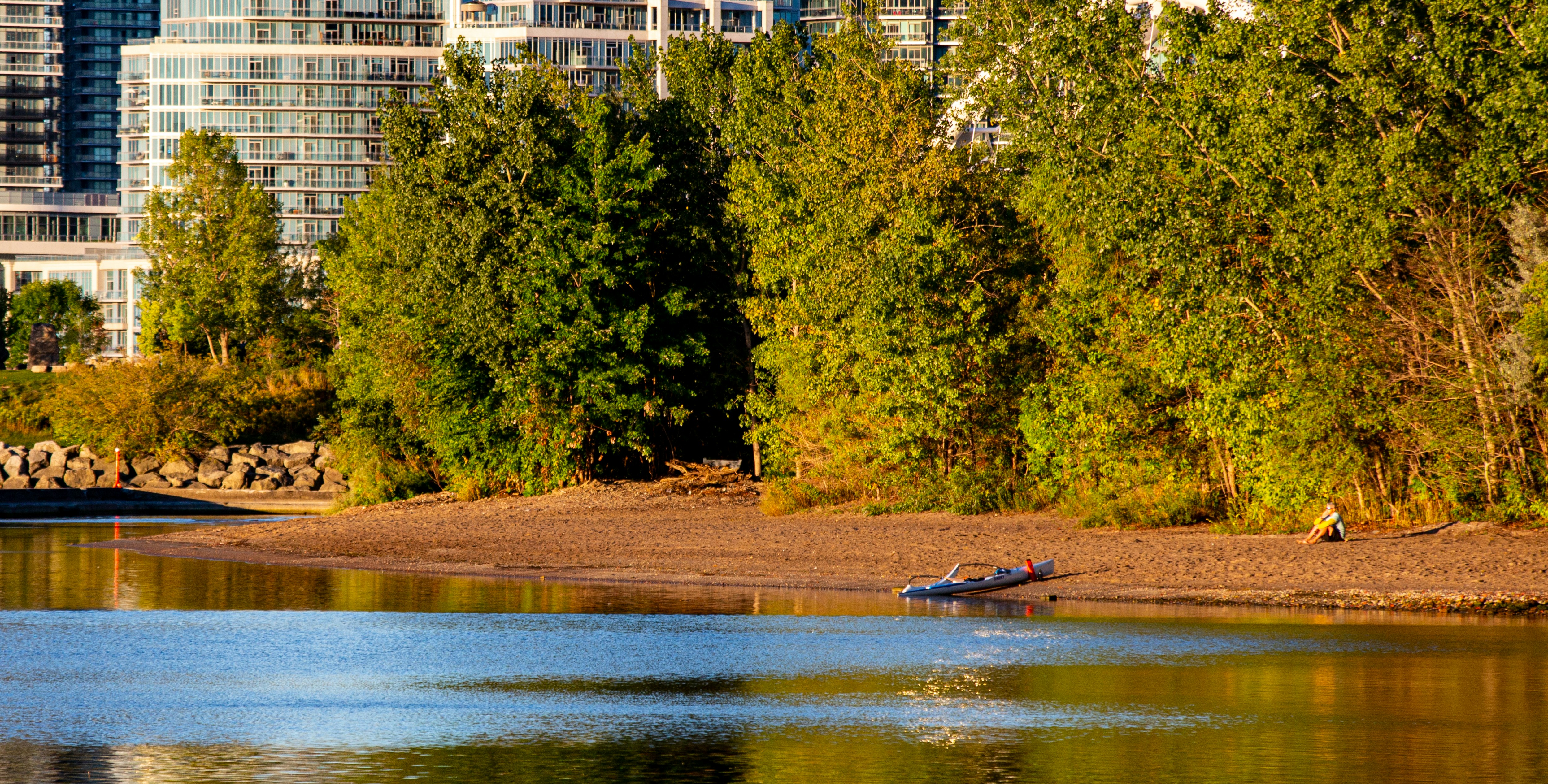 A small kayak rests on a sandy shore near trees.