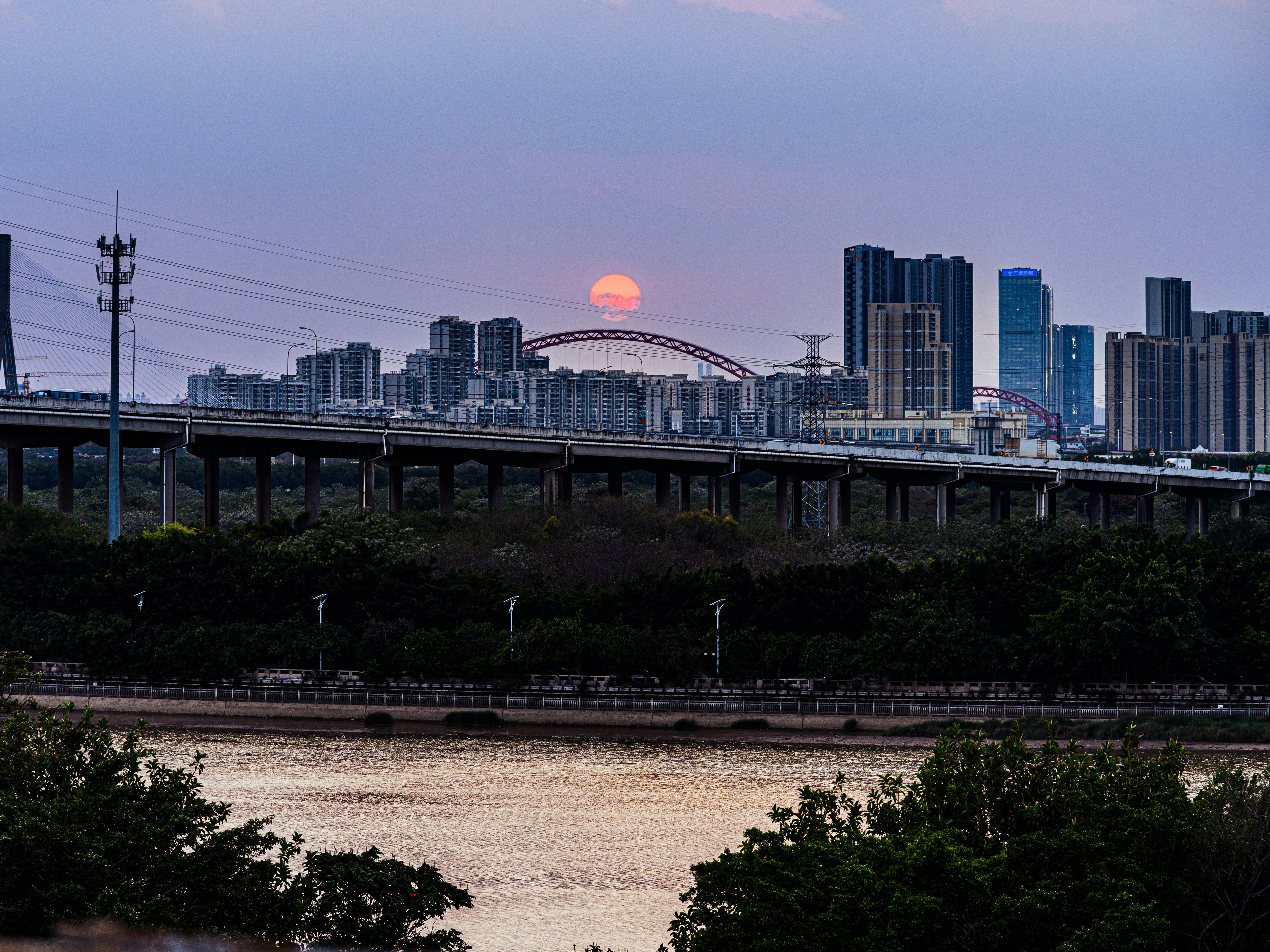 Sonnenuntergang über einer modernen Stadtlandschaft mit einer Brücke.