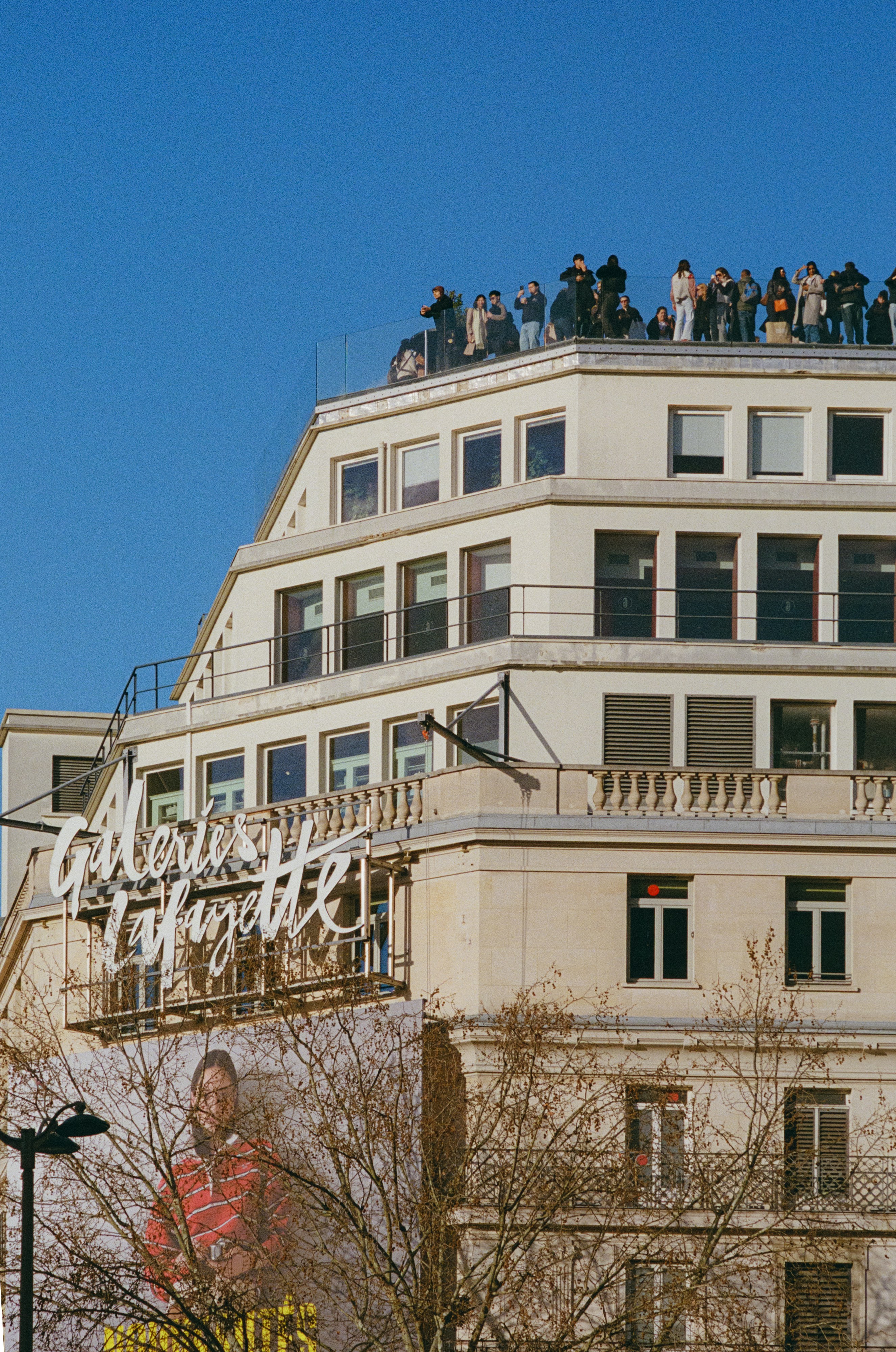 People gather on a building rooftop overlooking a billboard.