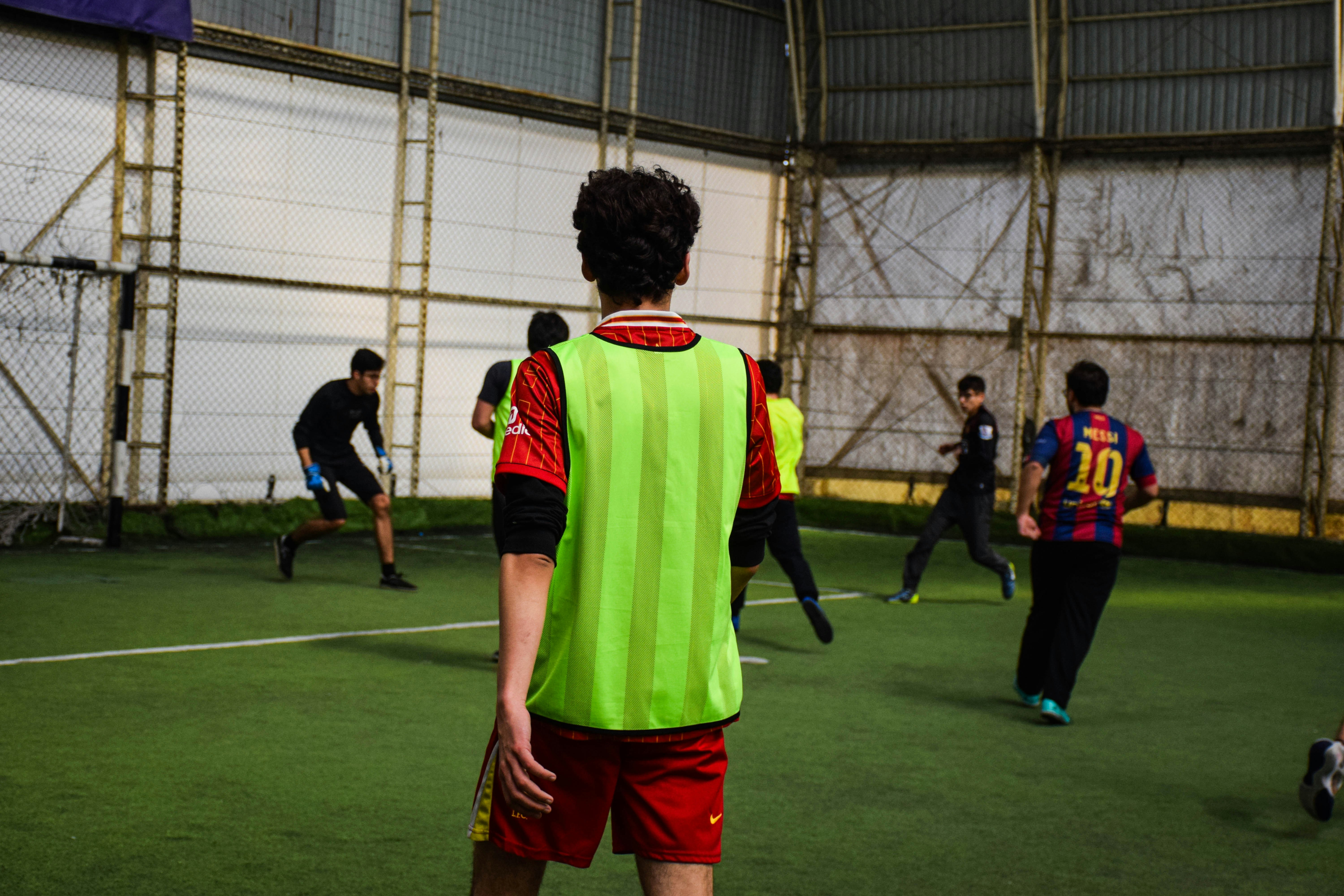 Pria muda bermain sepak bola dalam ruangan di lapangan hijau.