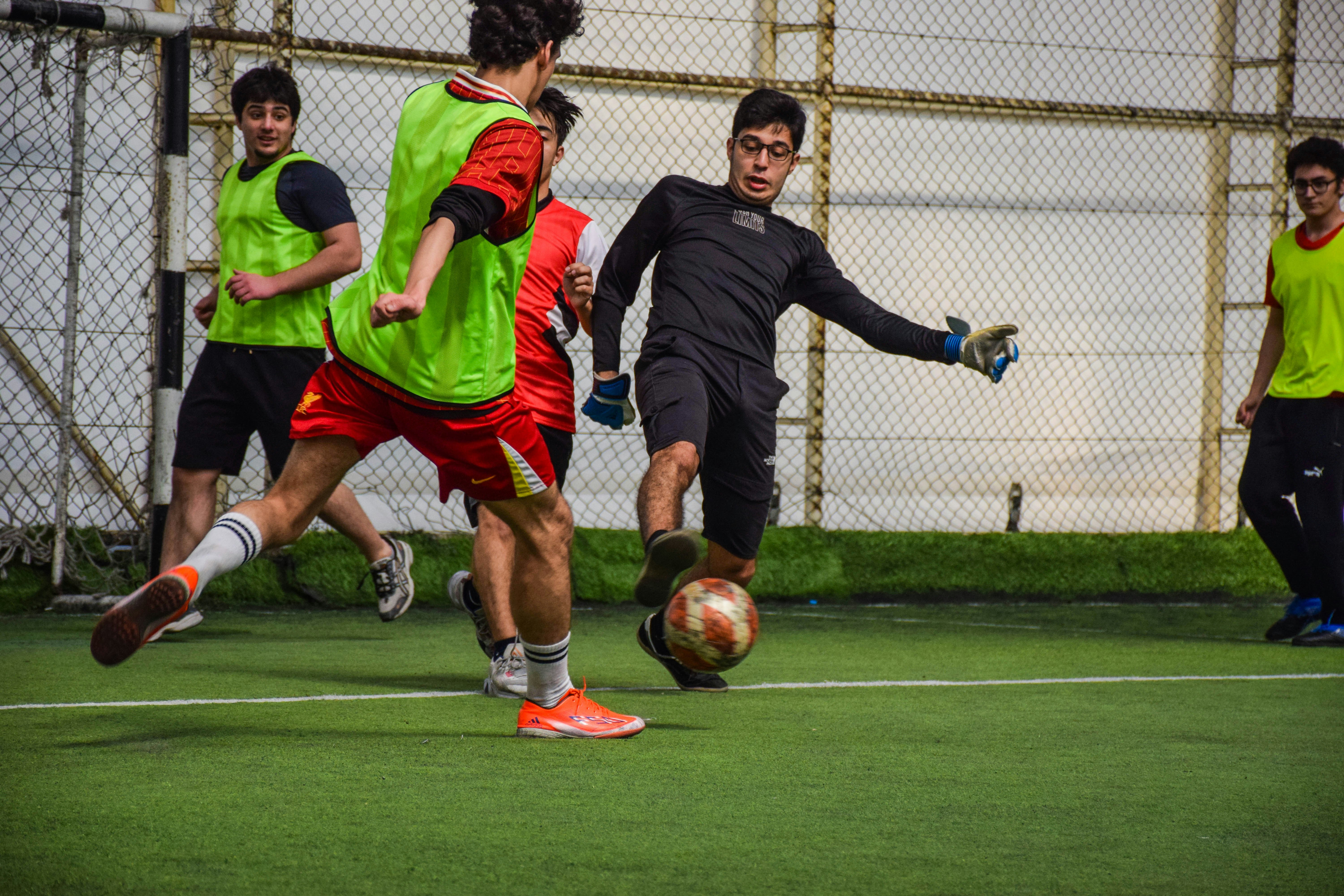 Pria muda bermain sepak bola di dalam ruangan di lapangan hijau.