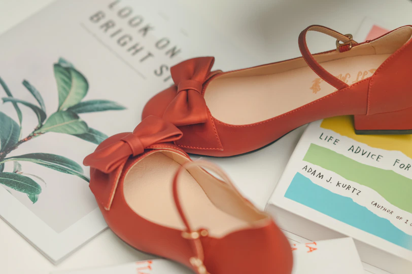 Red ballet flats with bows sit near books.