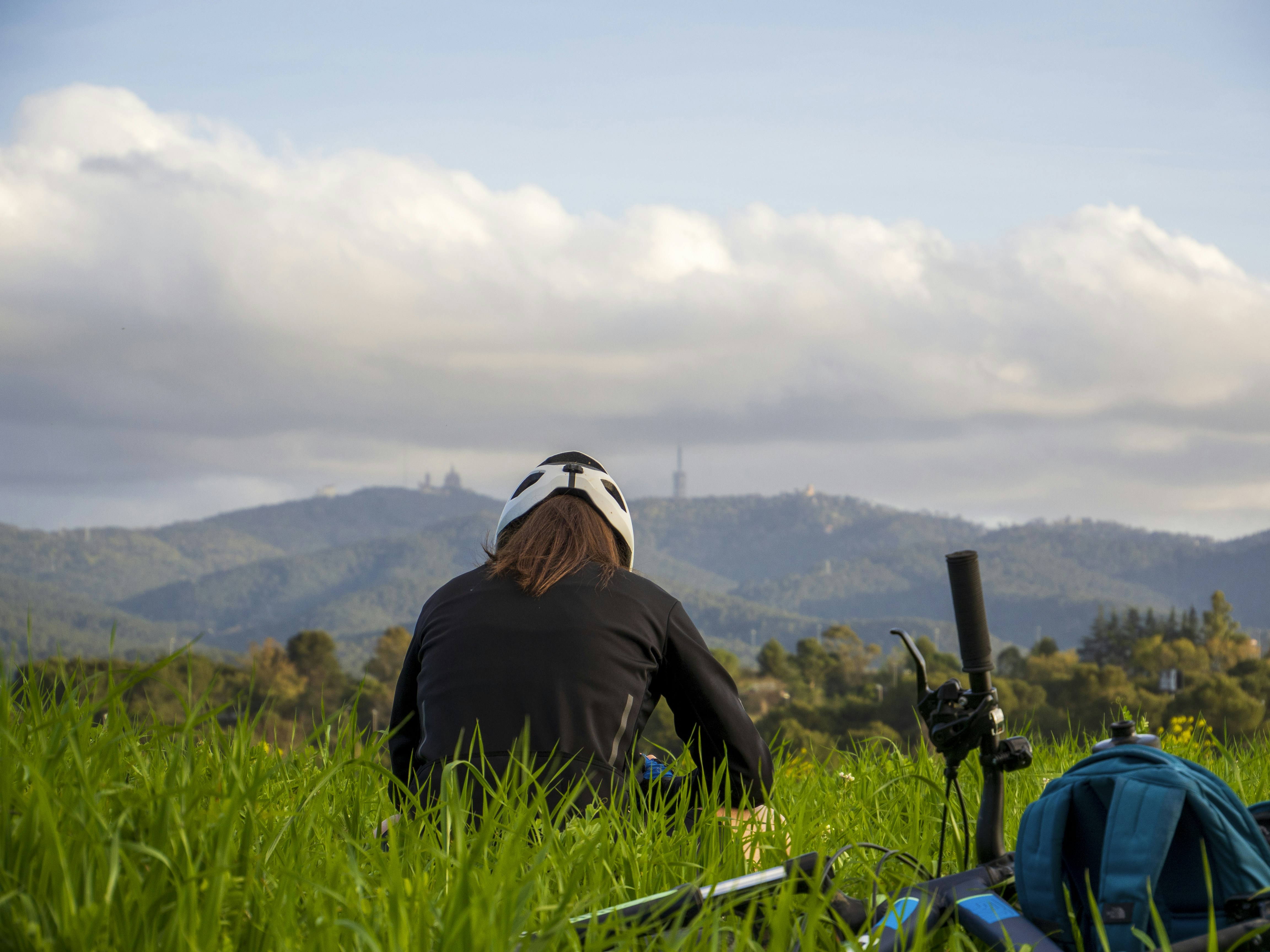 Person in helmet sits in a grassy field with mountains.