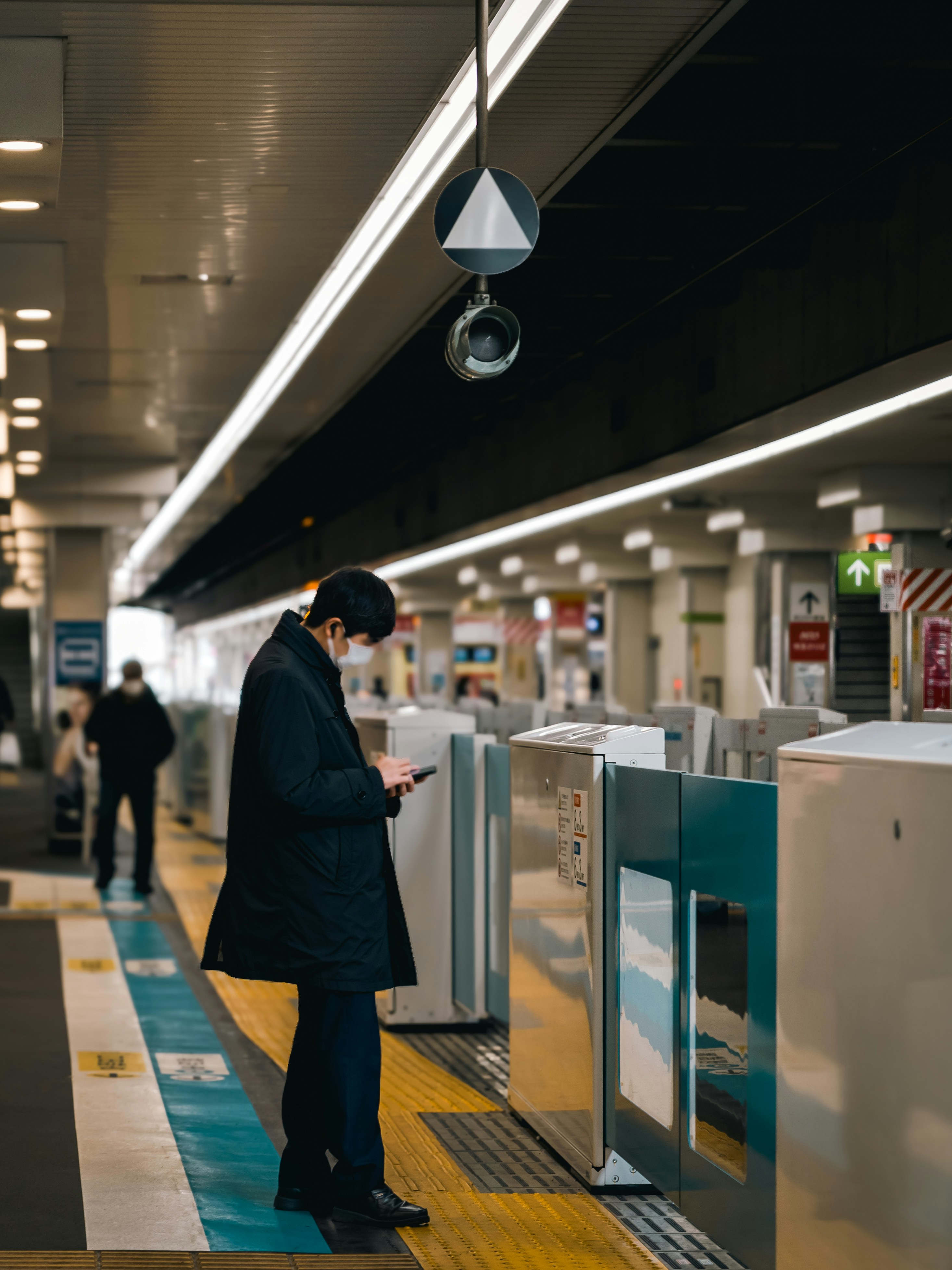Man wearing mask checks phone at train station entrance.