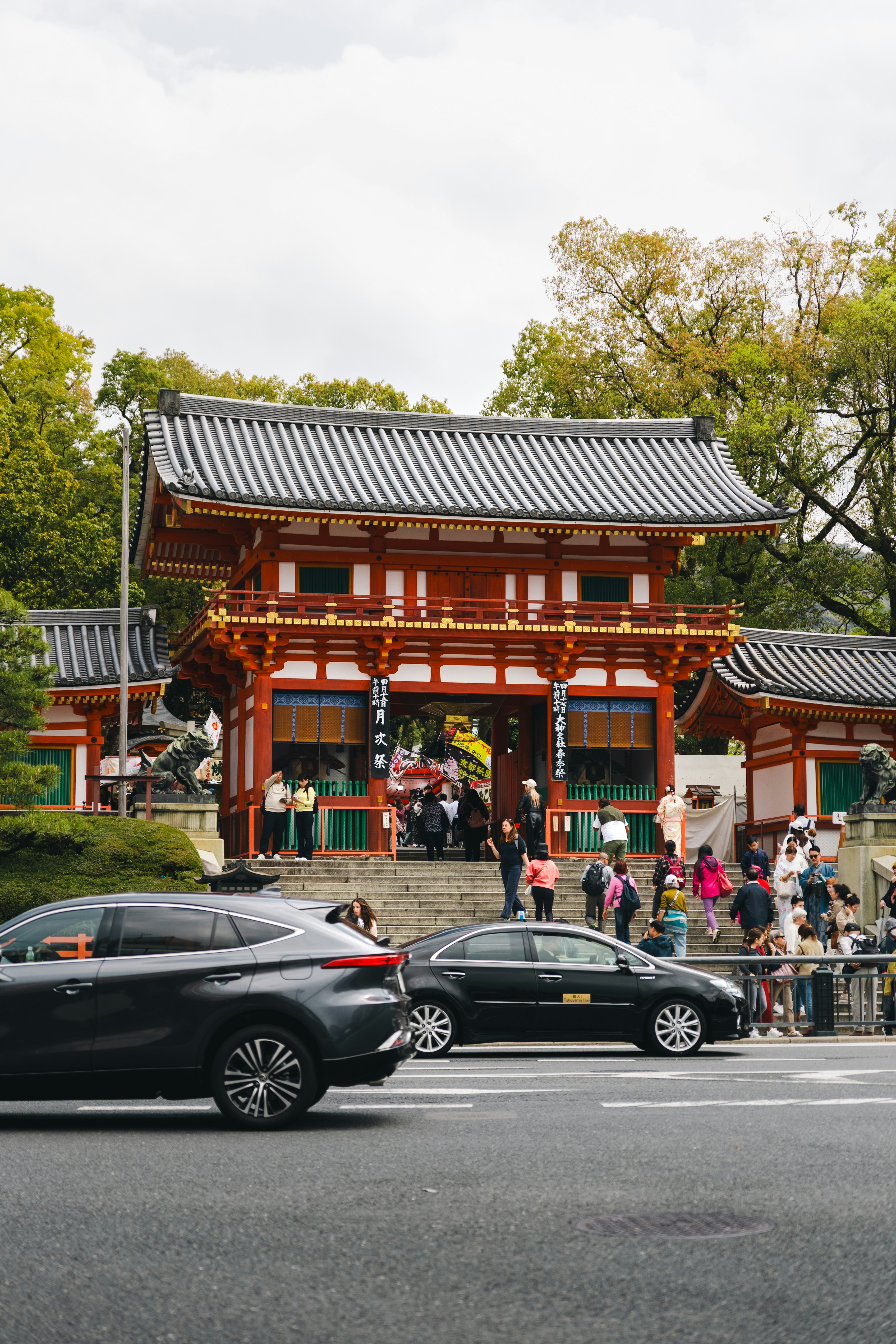 People entering a red japanese temple with cars nearby
