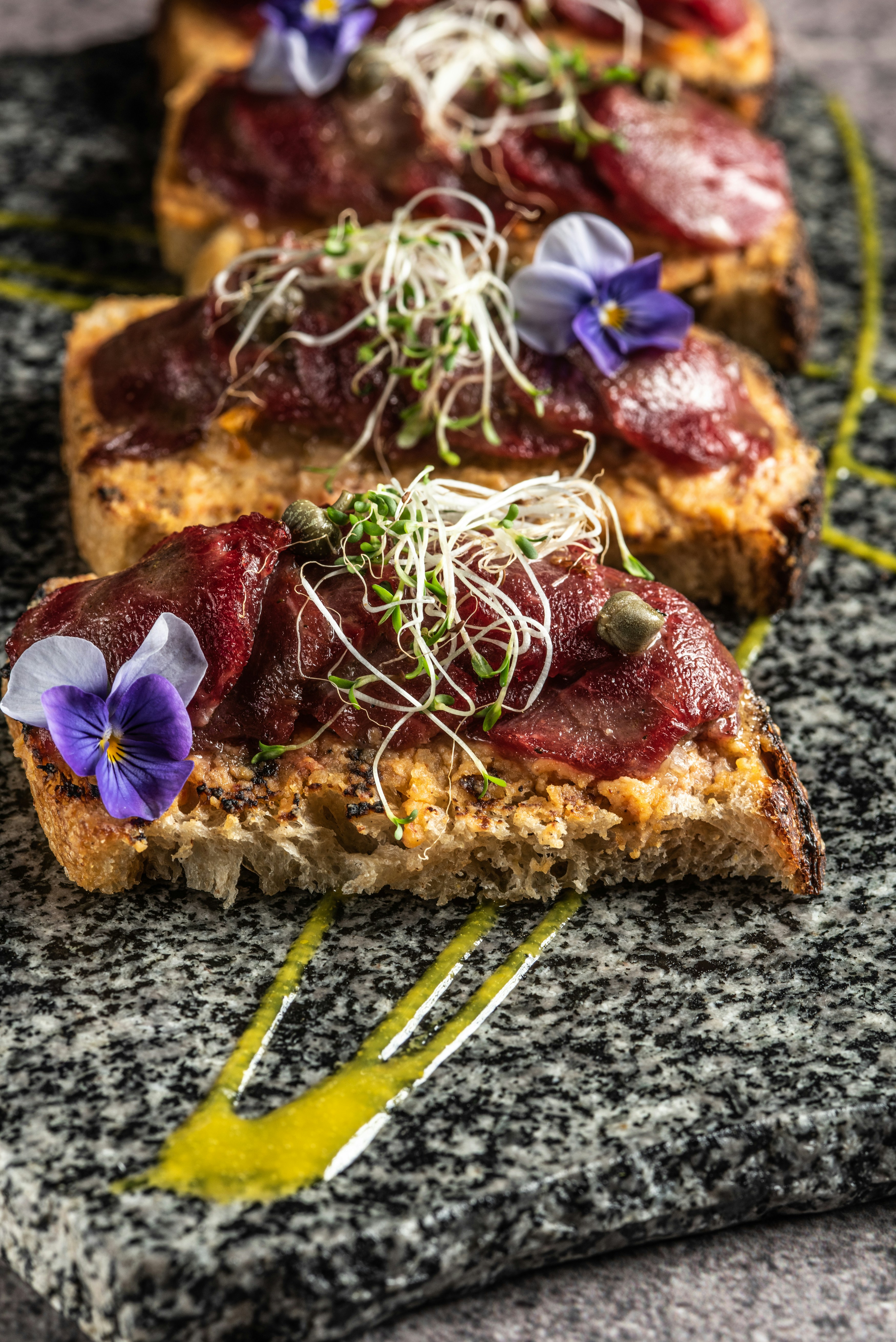 Fette di pane tostate con carne guarnita, germogli e fiori.