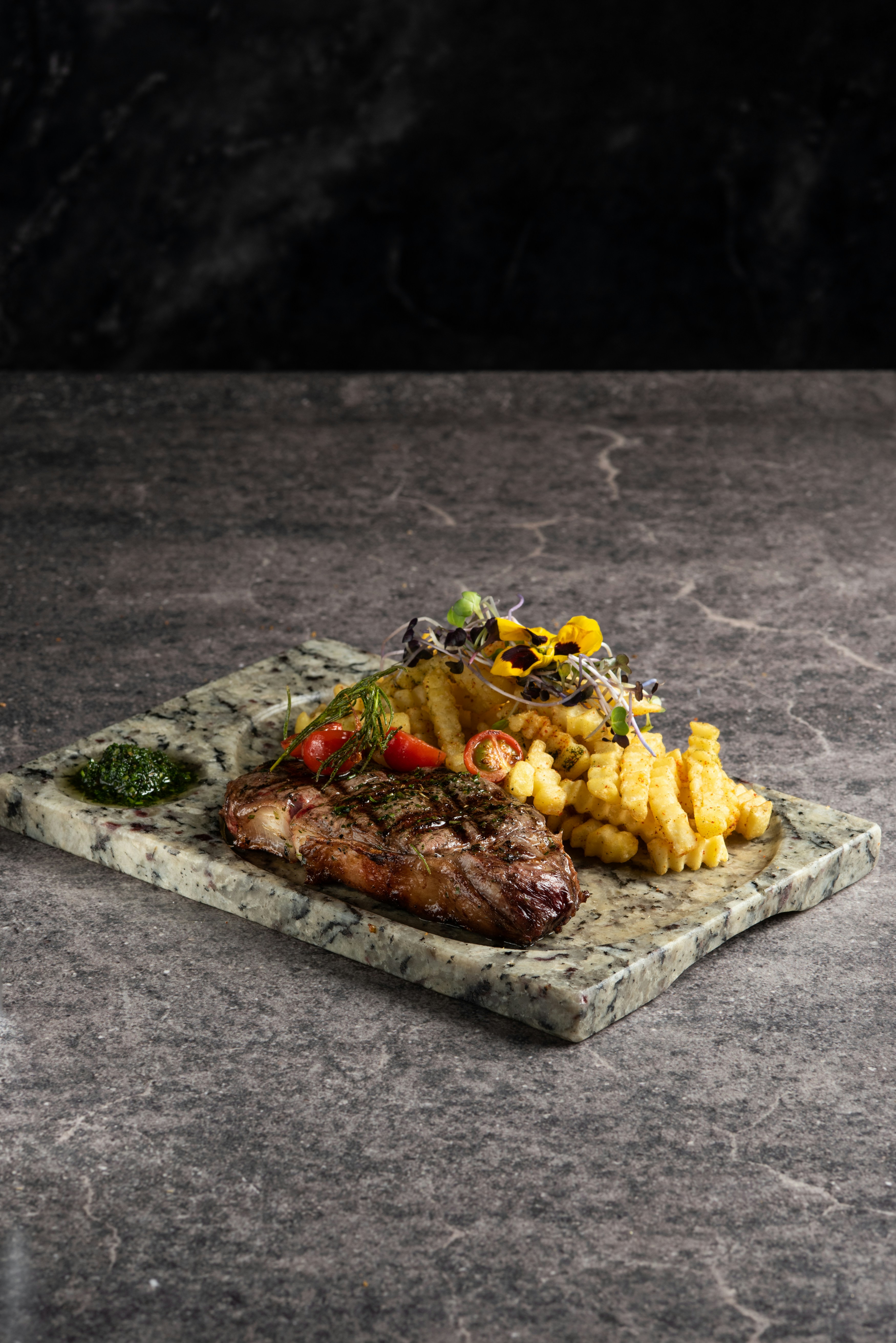 Bistecca alla griglia con patatine e decorazione su una lastra di marmo