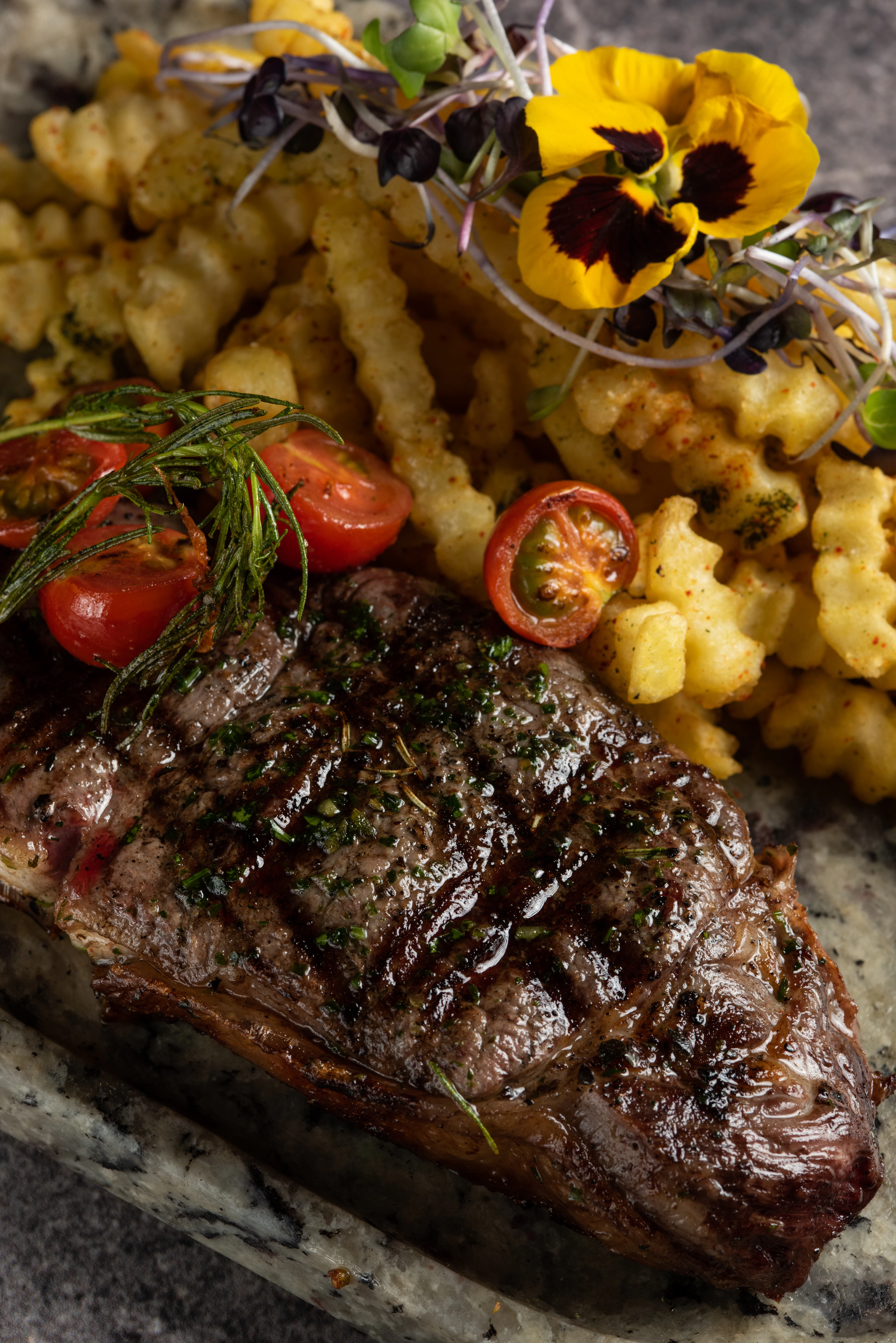 A sliced steak with roast tomatoes and crinkle-cut fries on a dark plate
