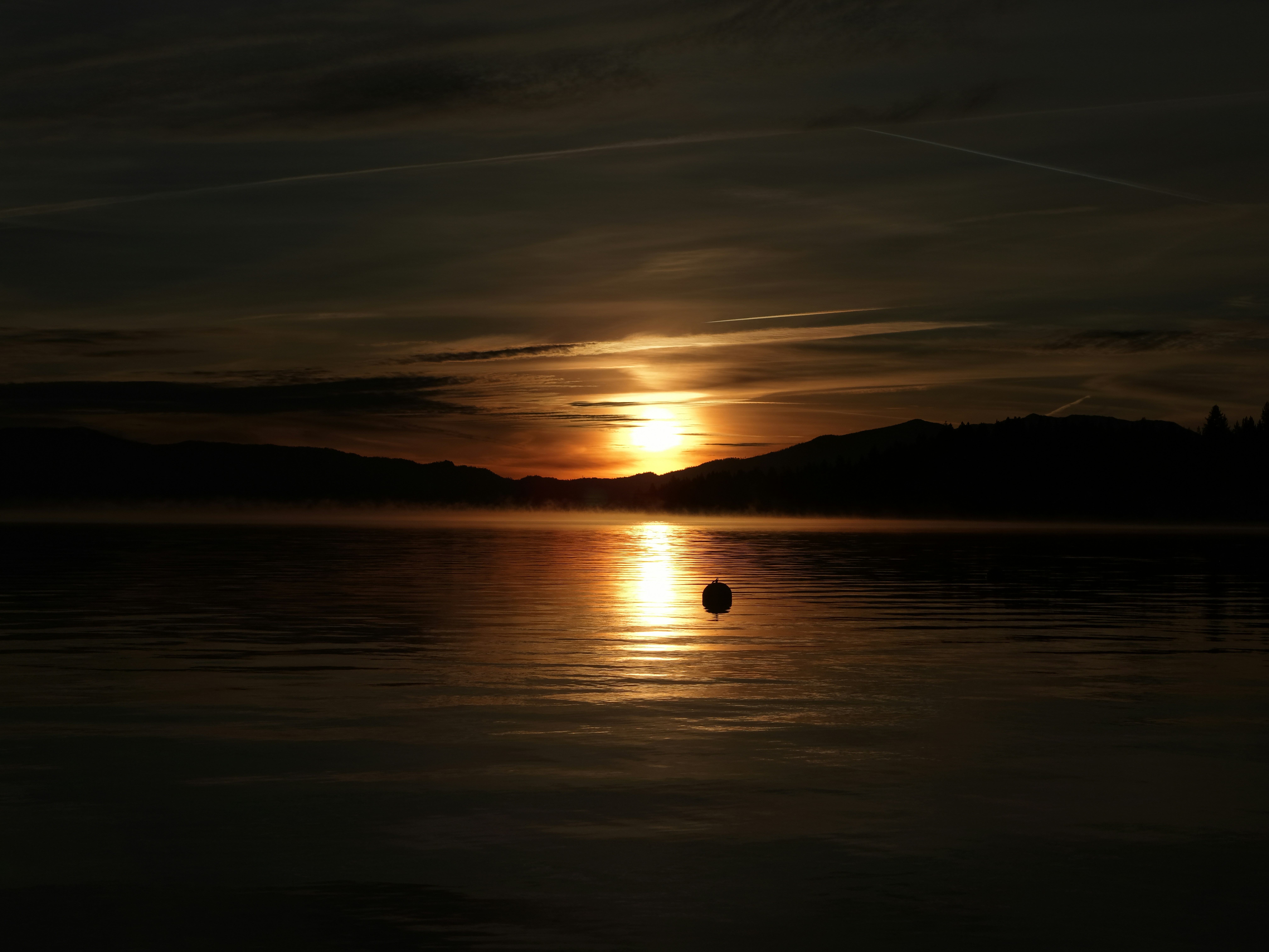 Atardecer sobre un lago tranquilo con una sola boya.
