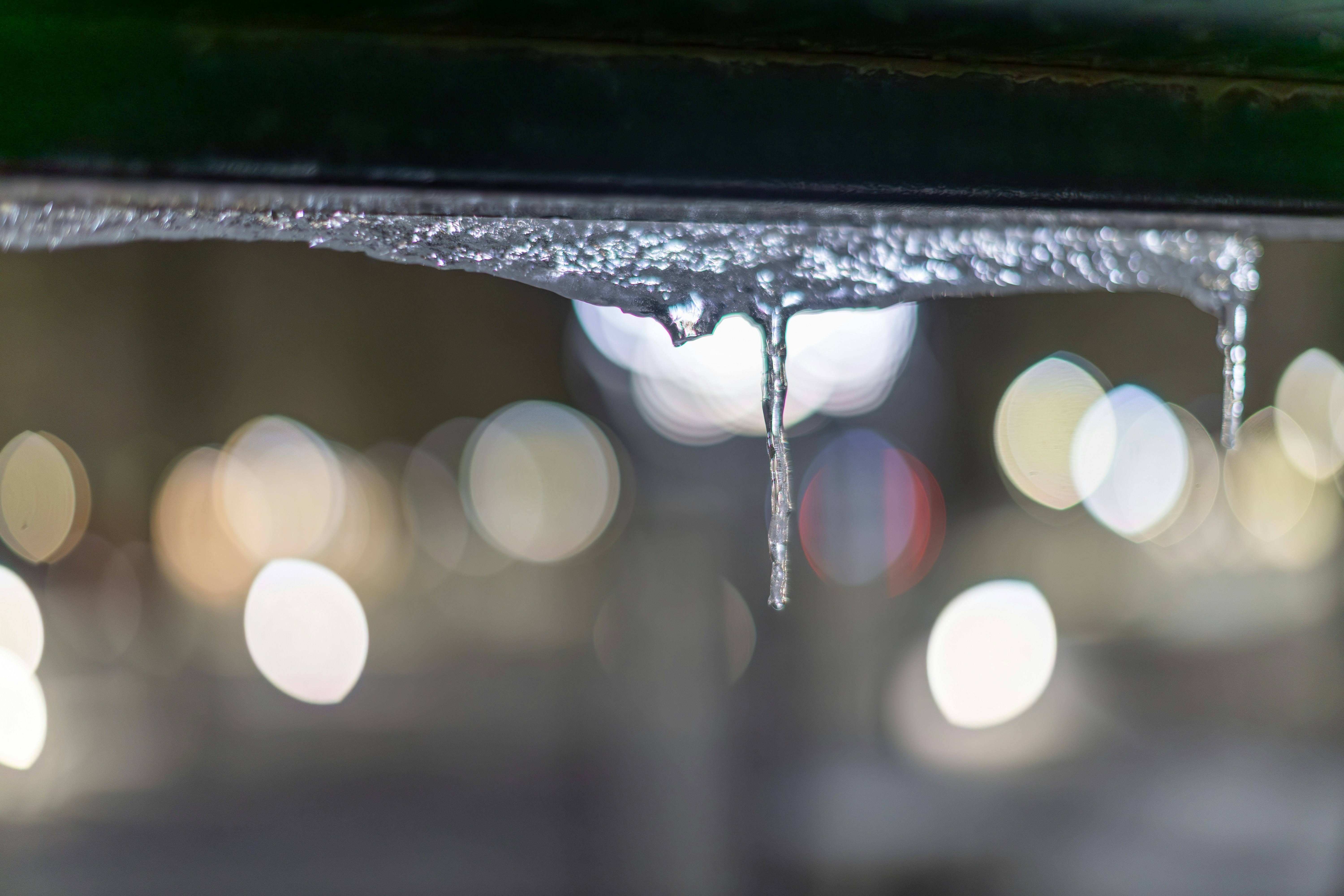 Eiszapfen tropften aus einem dunklen Überhang mit Bokeh-Lichtern.