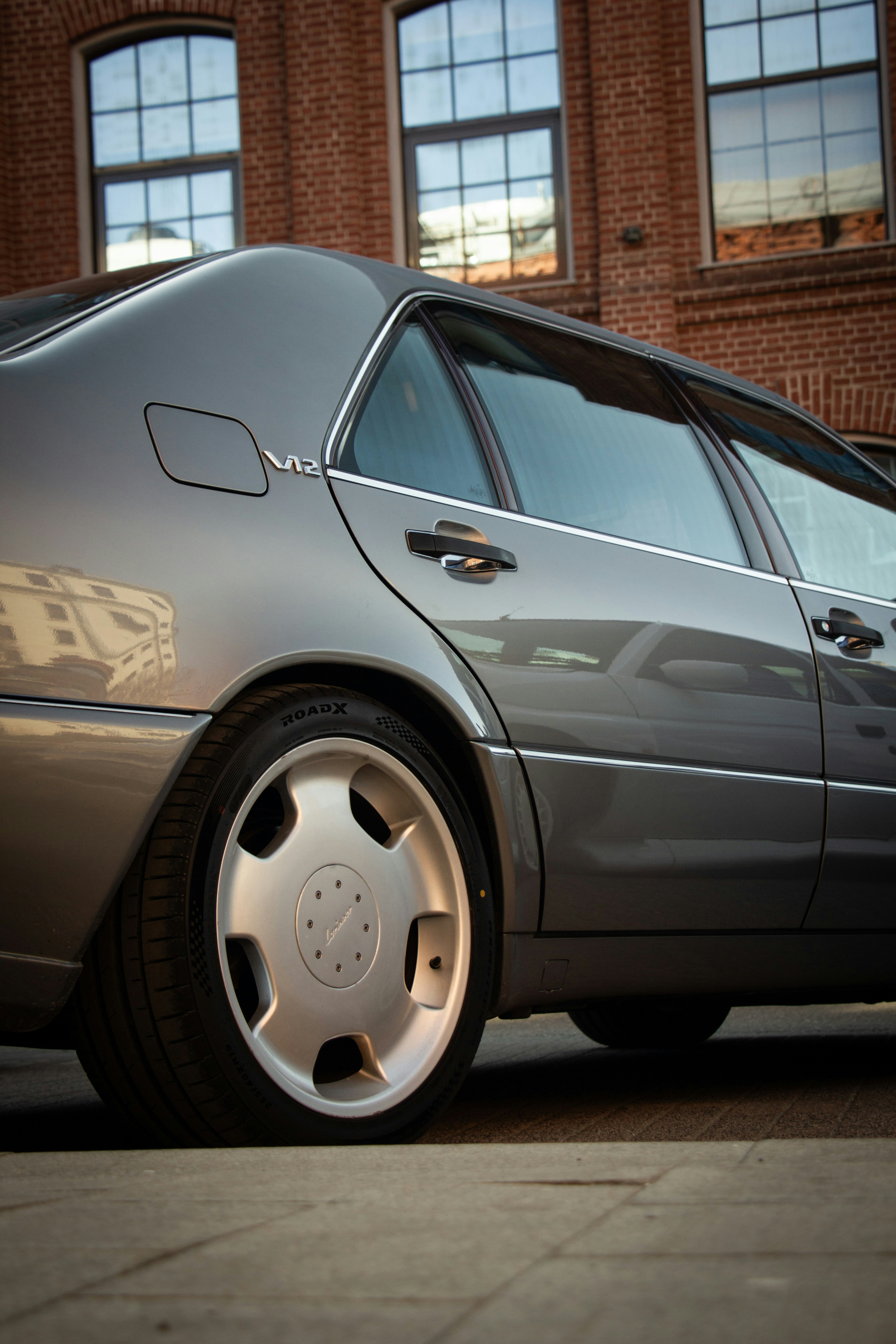 A grey luxury sedan parked near a brick building.