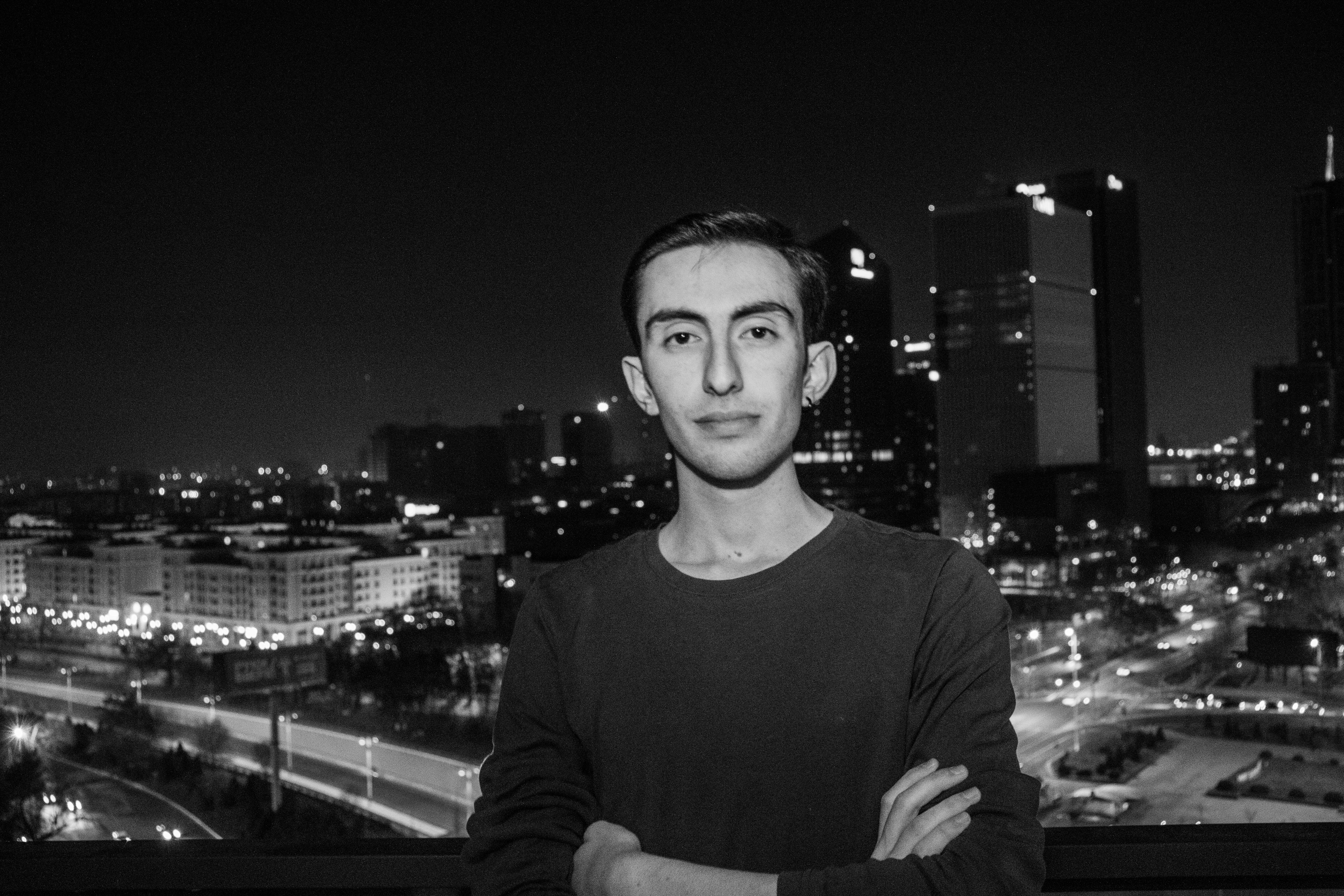 Homme debout, les bras croisés la nuit, avec la silhouette de la ville.