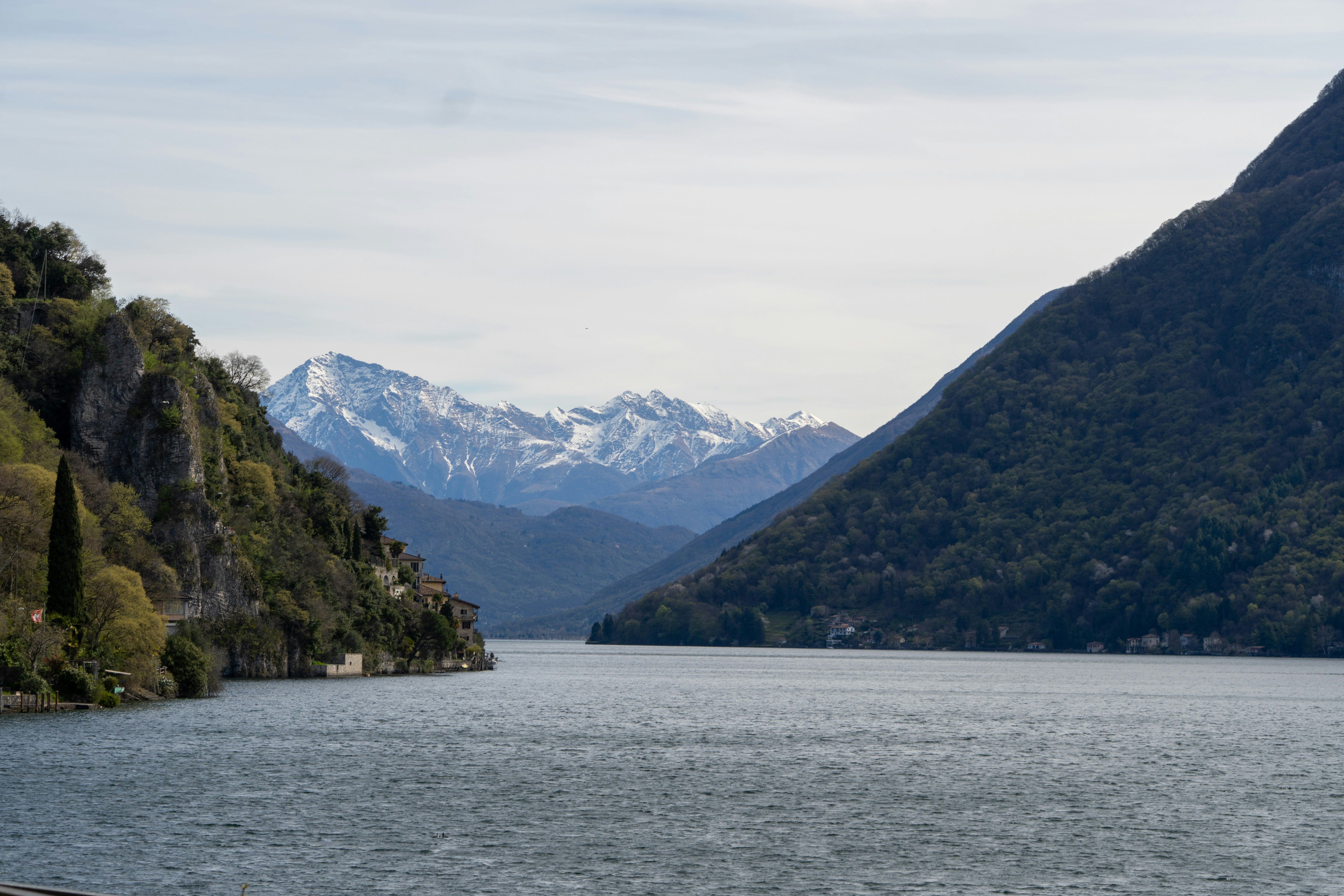 Calm lake between two tree-covered mountains with snow peaks
