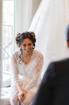 A smiling bride in a lace robe looks at someone