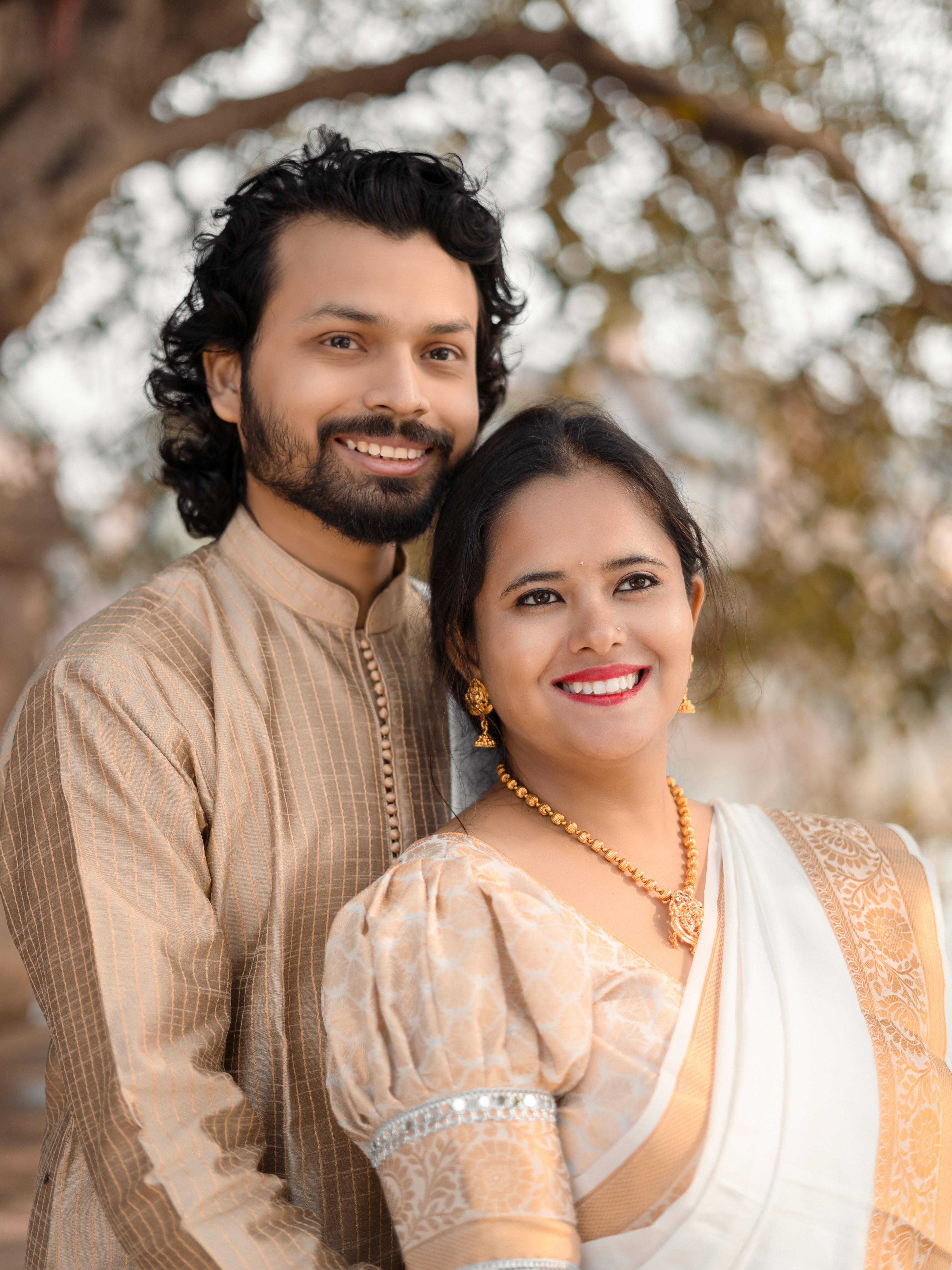 A smiling couple poses outdoors in traditional attire.