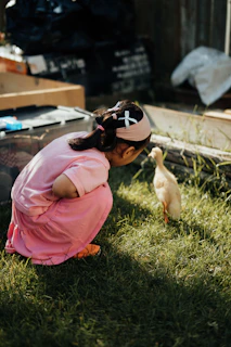 Girl in pink dress curiously observing a duckling duckling.