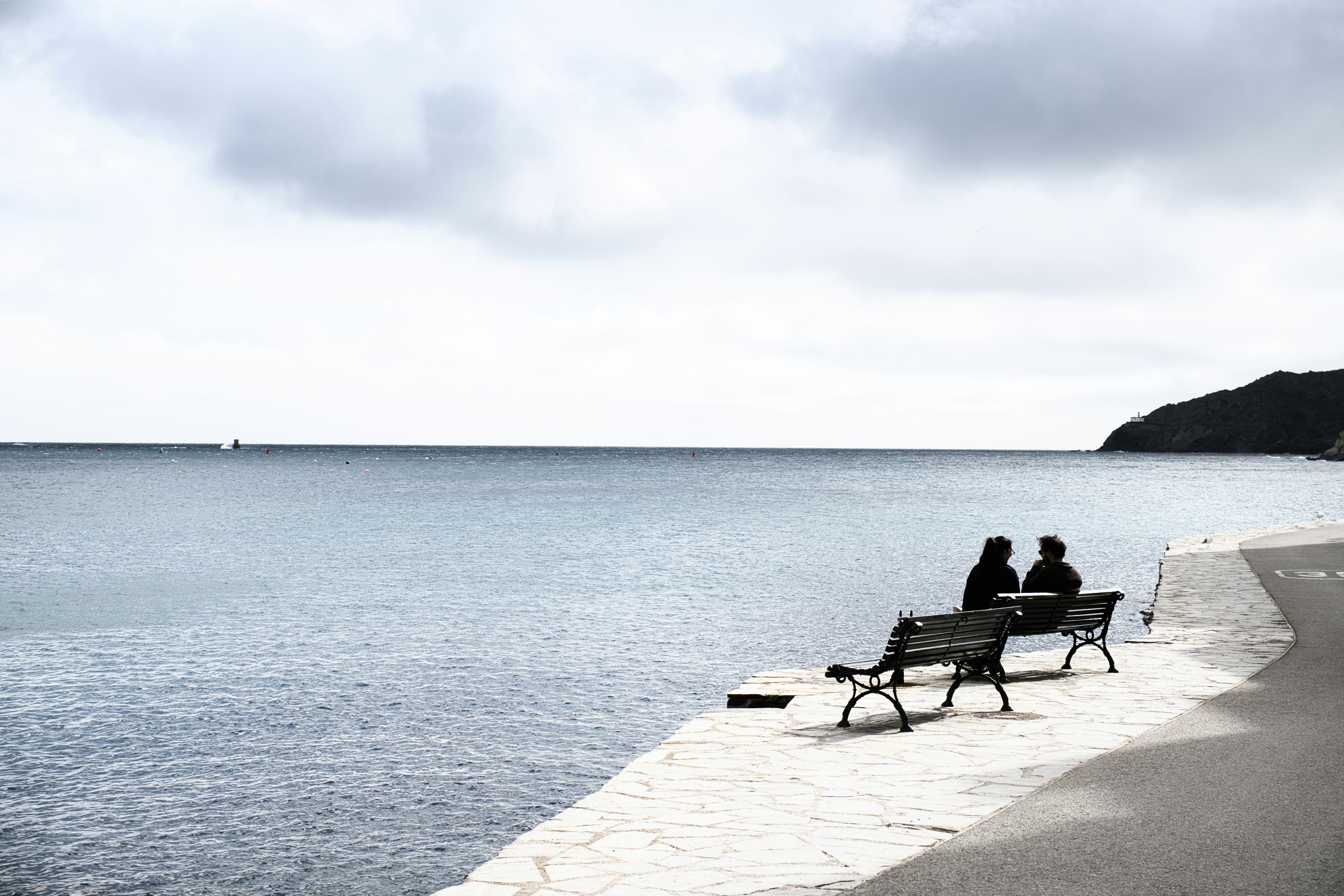Two people sit on a bench by the sea.