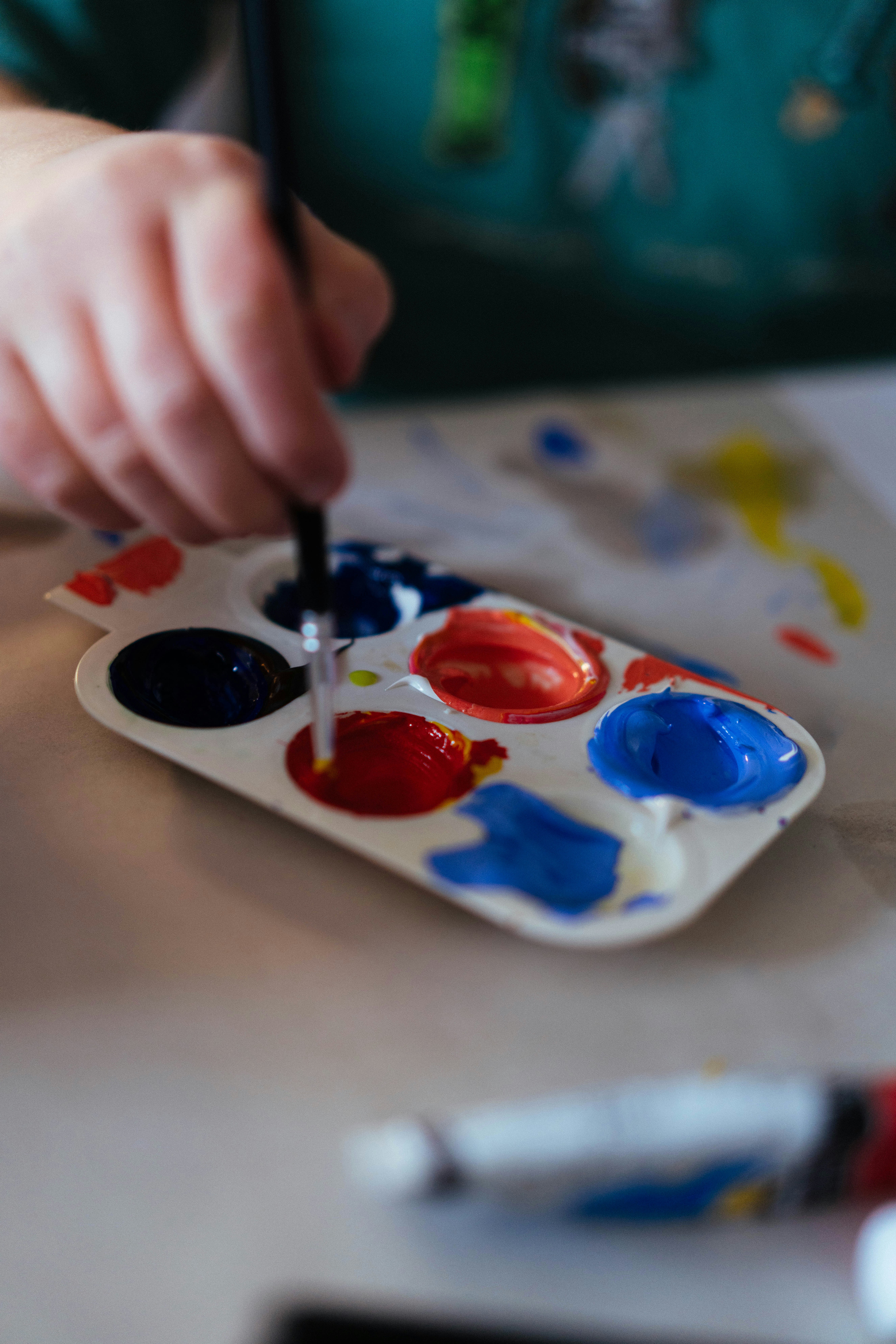 A hand dips a brush into a colorful paint palette.