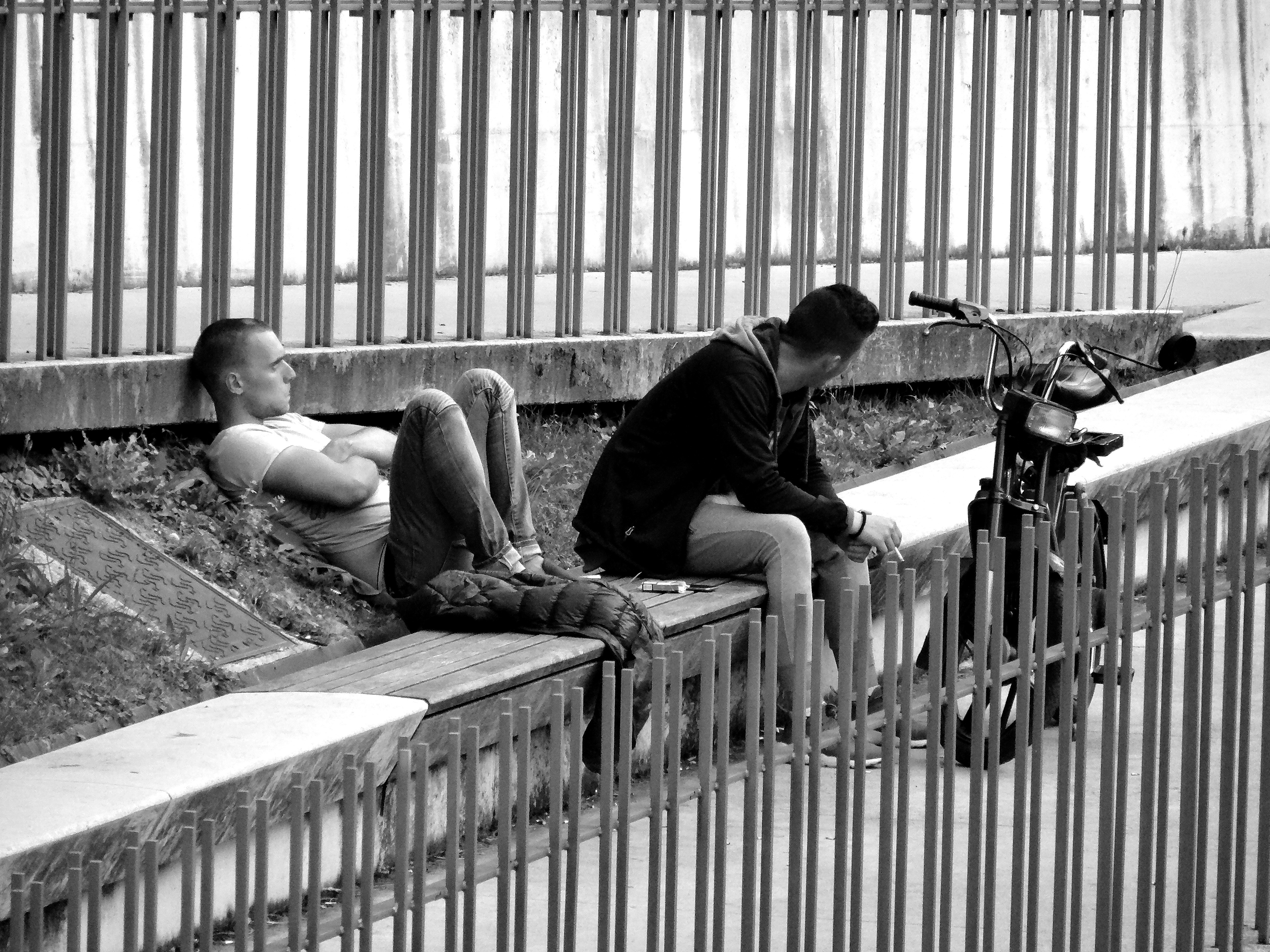 Two people sitting by a metal fence