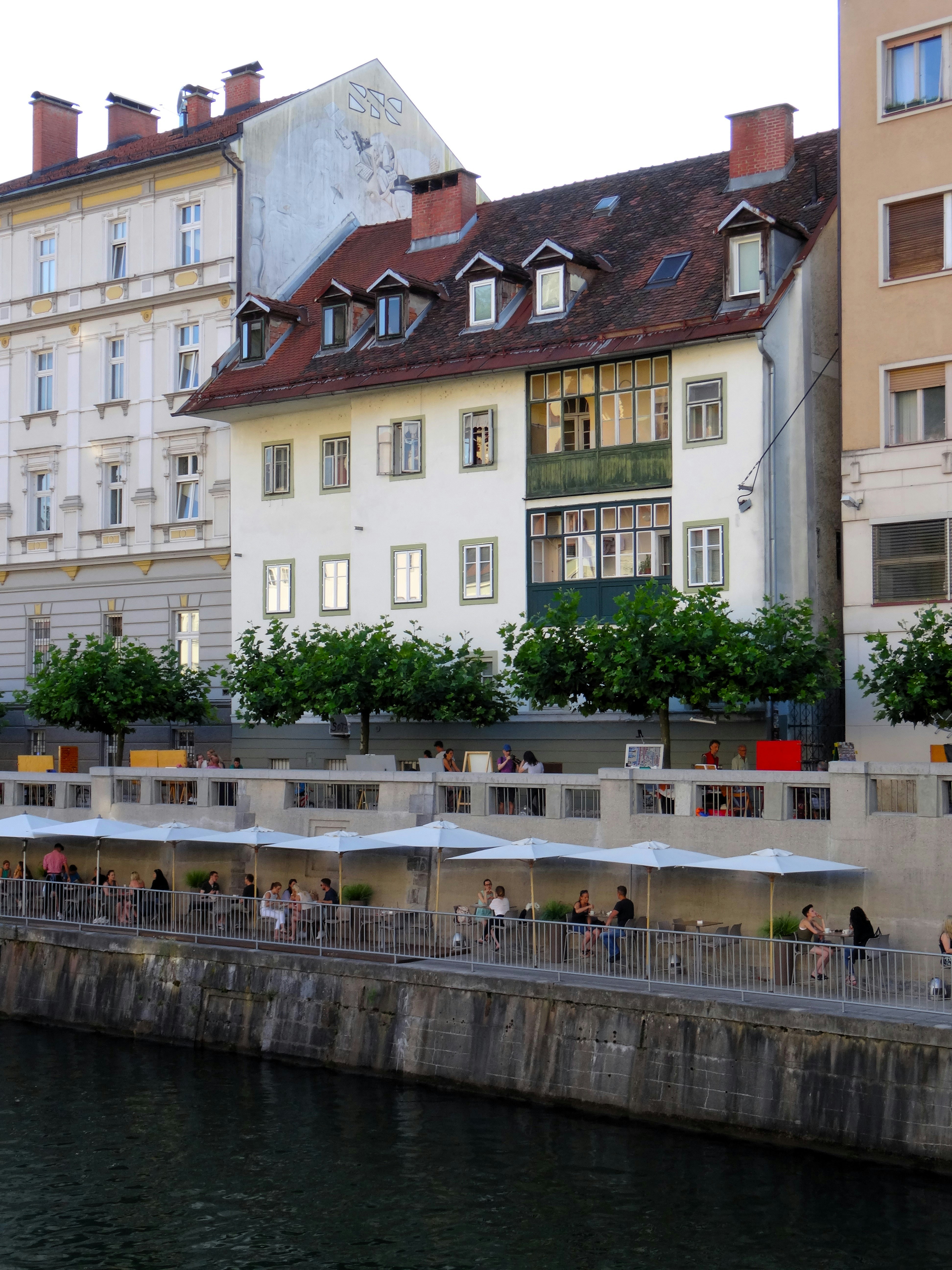 Buildings line a river with outdoor seating and umbrellas.