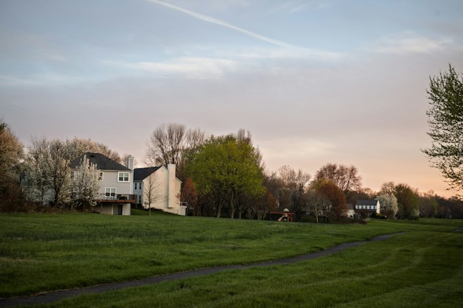 A suburban neighborhood with houses and trees at dusk, representing the HOA communities whose common-area grass falls under the new turf fine rules