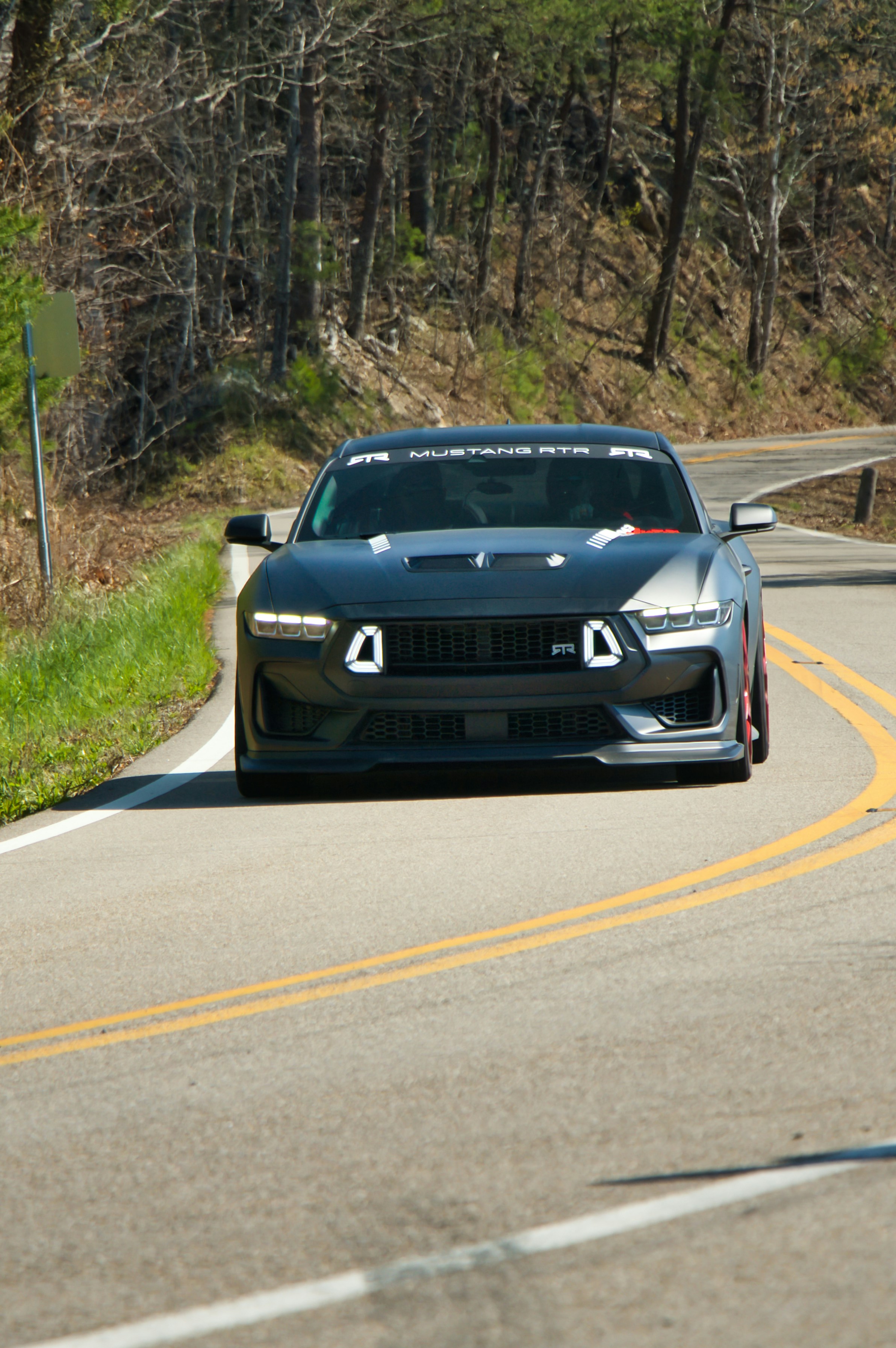 Ein dunkler Sportwagen fährt auf einer kurvigen Straße.